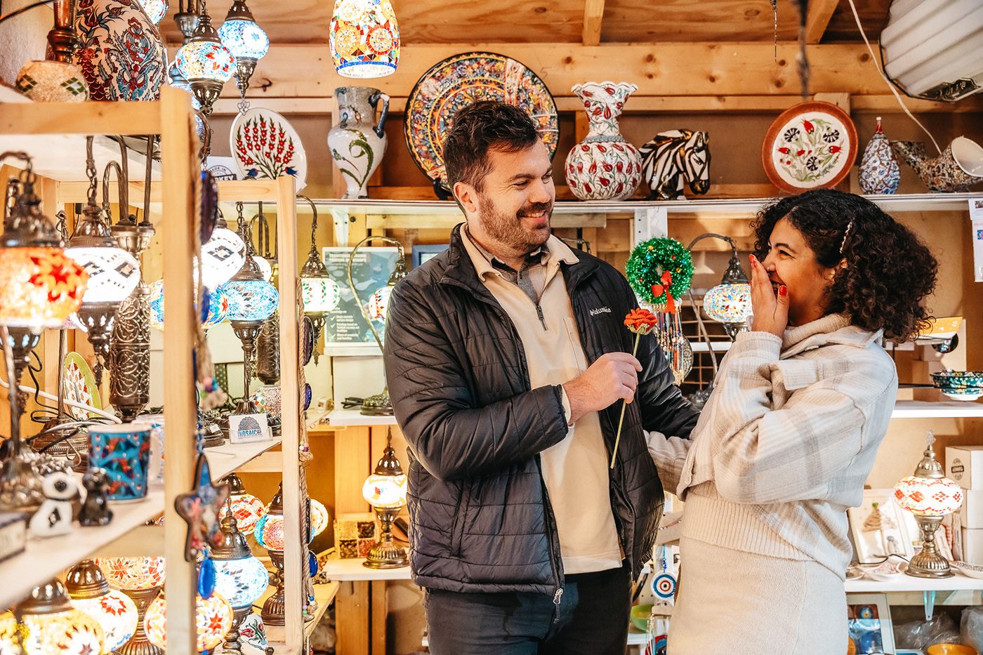 A couple shares a joyful moment while shopping in a festive holiday market with decorative lights.