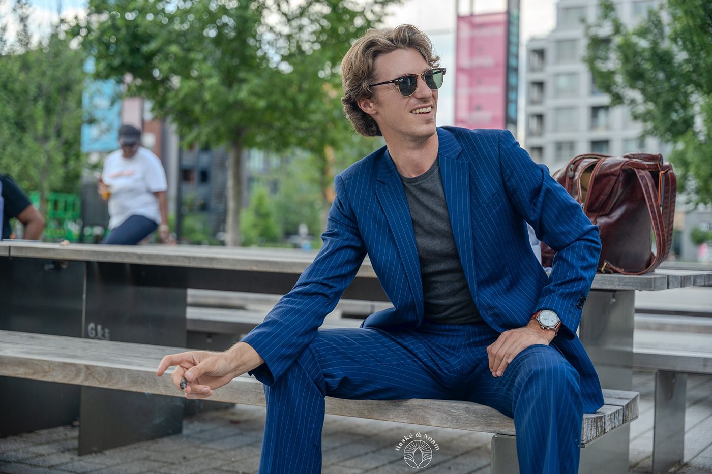 A person in a blue suit and sunglasses sitting casually on an outdoor bench.