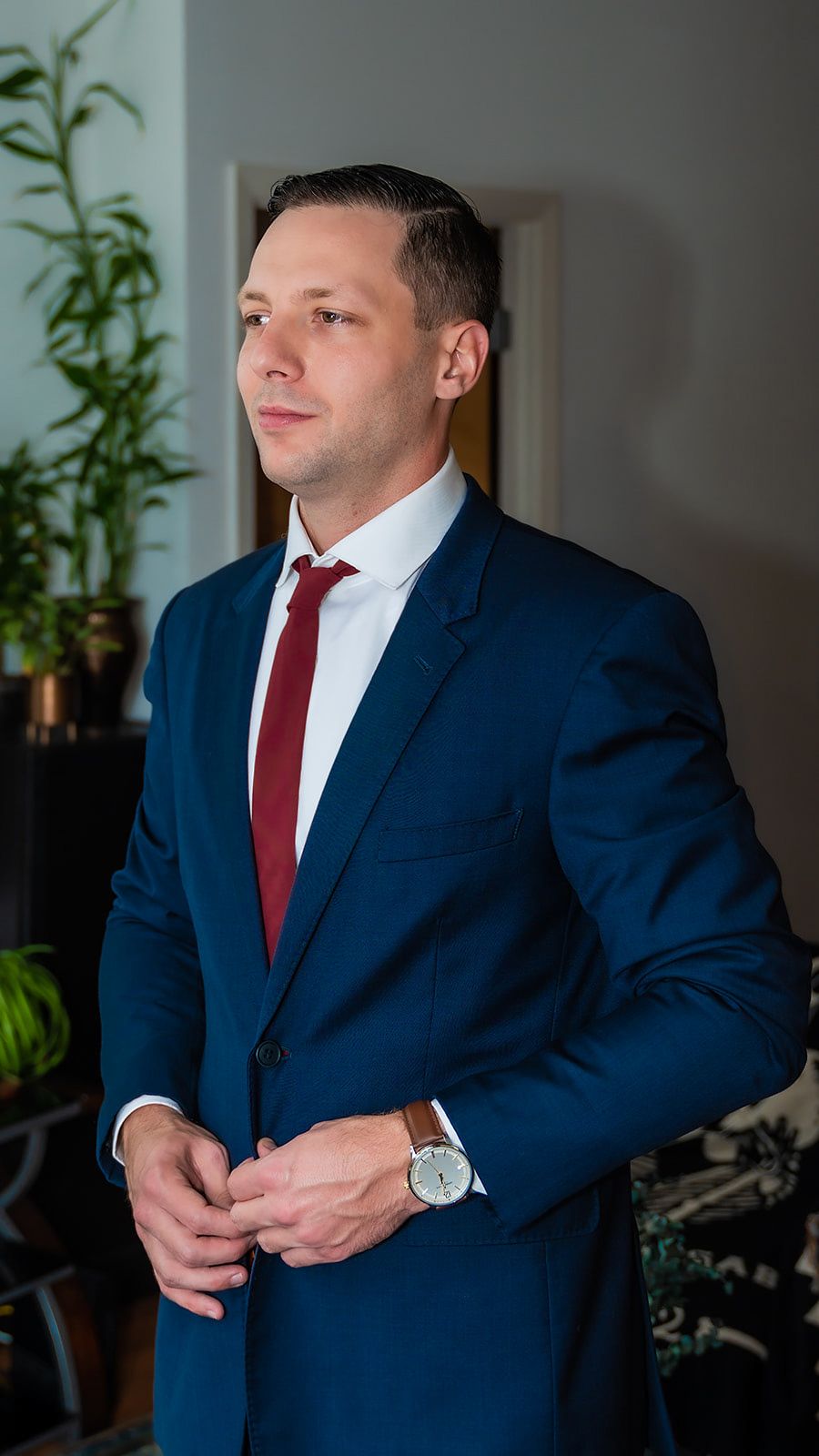 Professional portrait of a man in a navy suit with red tie adjusting his cuffs.