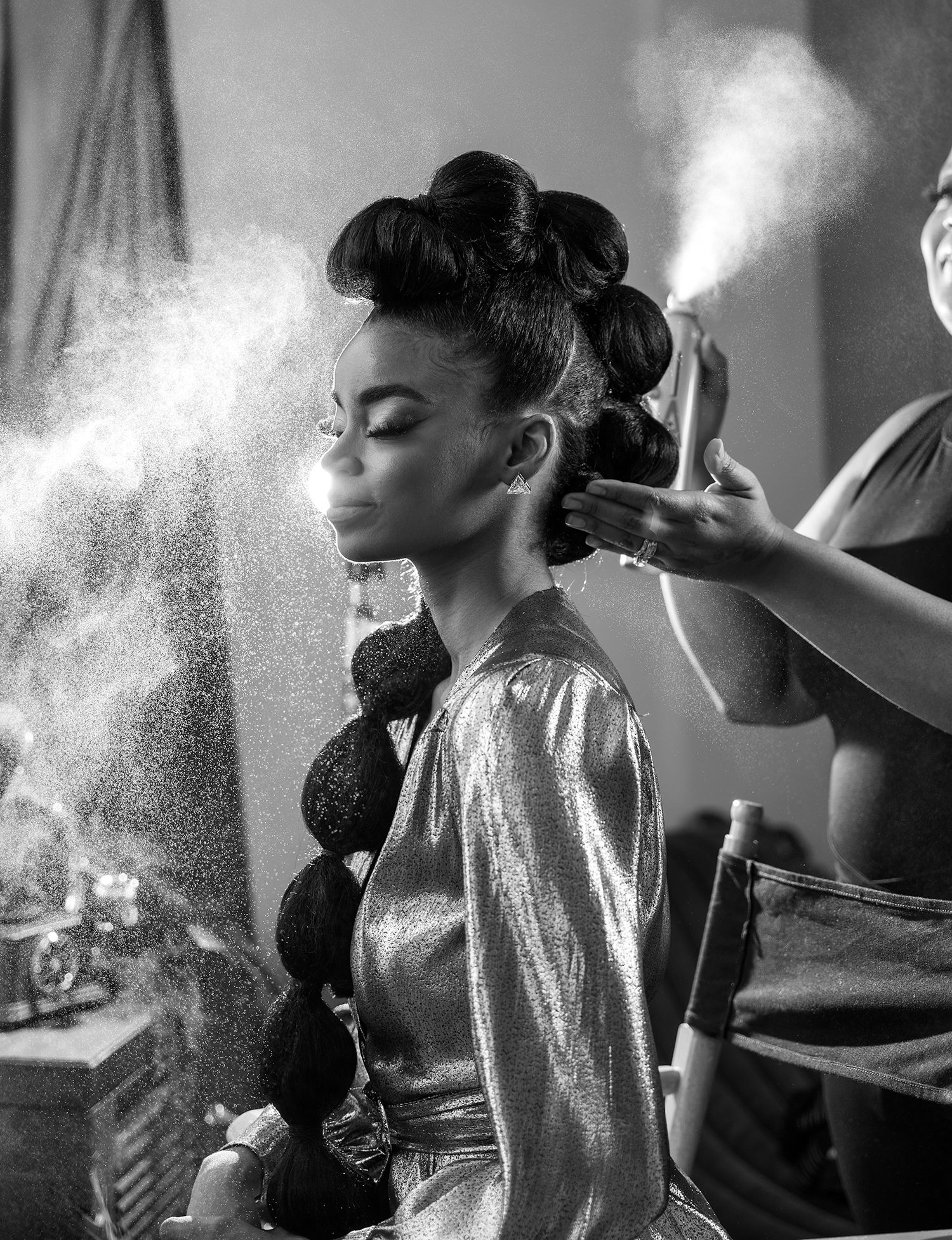 Black and white photo of a beauty styling session with dramatic lighting and spray effects.