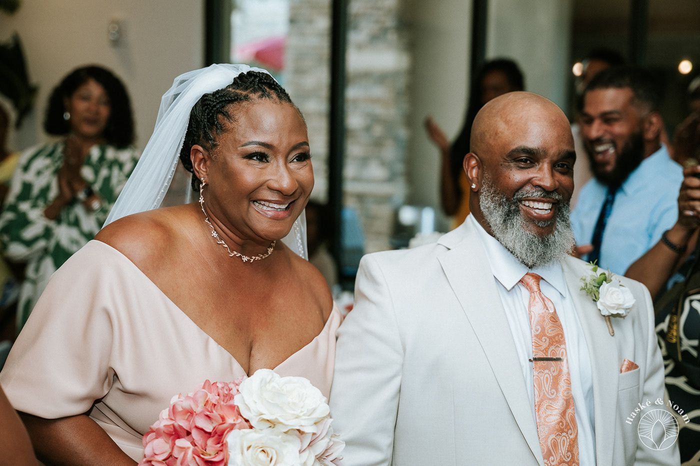 Wedding couple sharing happy moment at ceremony with pink and white floral bouquet.