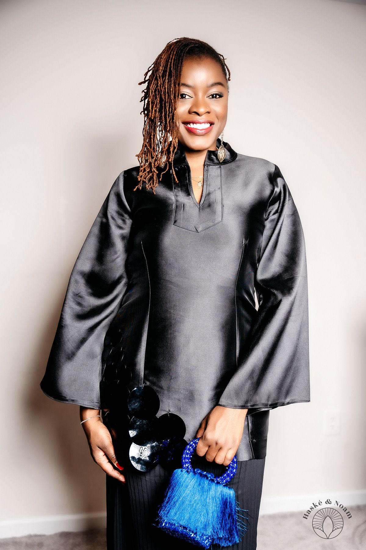 Person wearing elegant black silk top with bell sleeves holding blue tassel accessory.