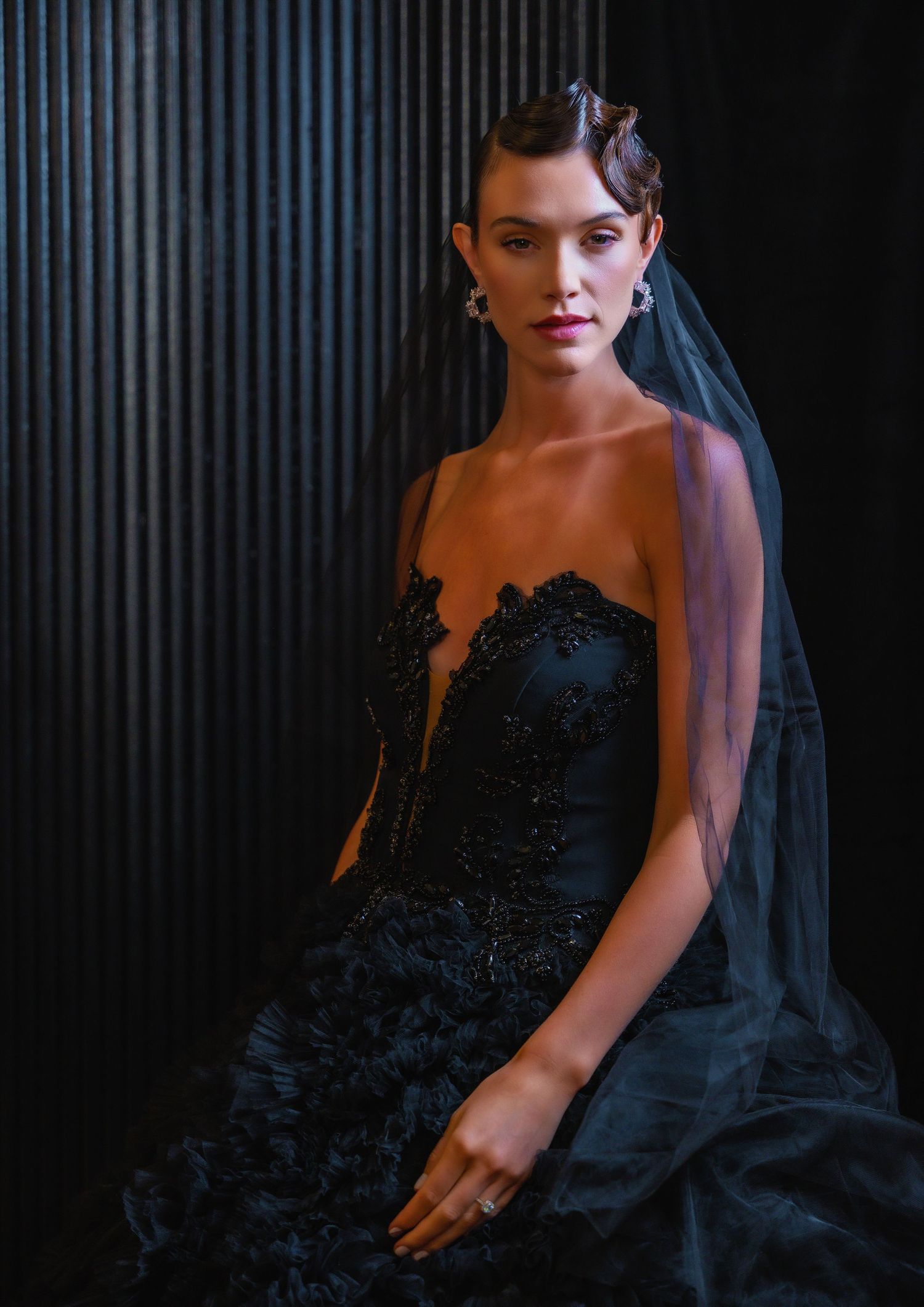 A moody fashion portrait showcasing a black wedding gown with delicate lace details against dark walls.