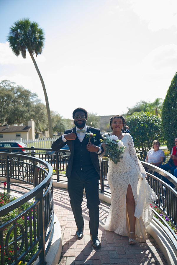 Wedding couple walking along a curved pathway with palm trees and blue sky in the background.