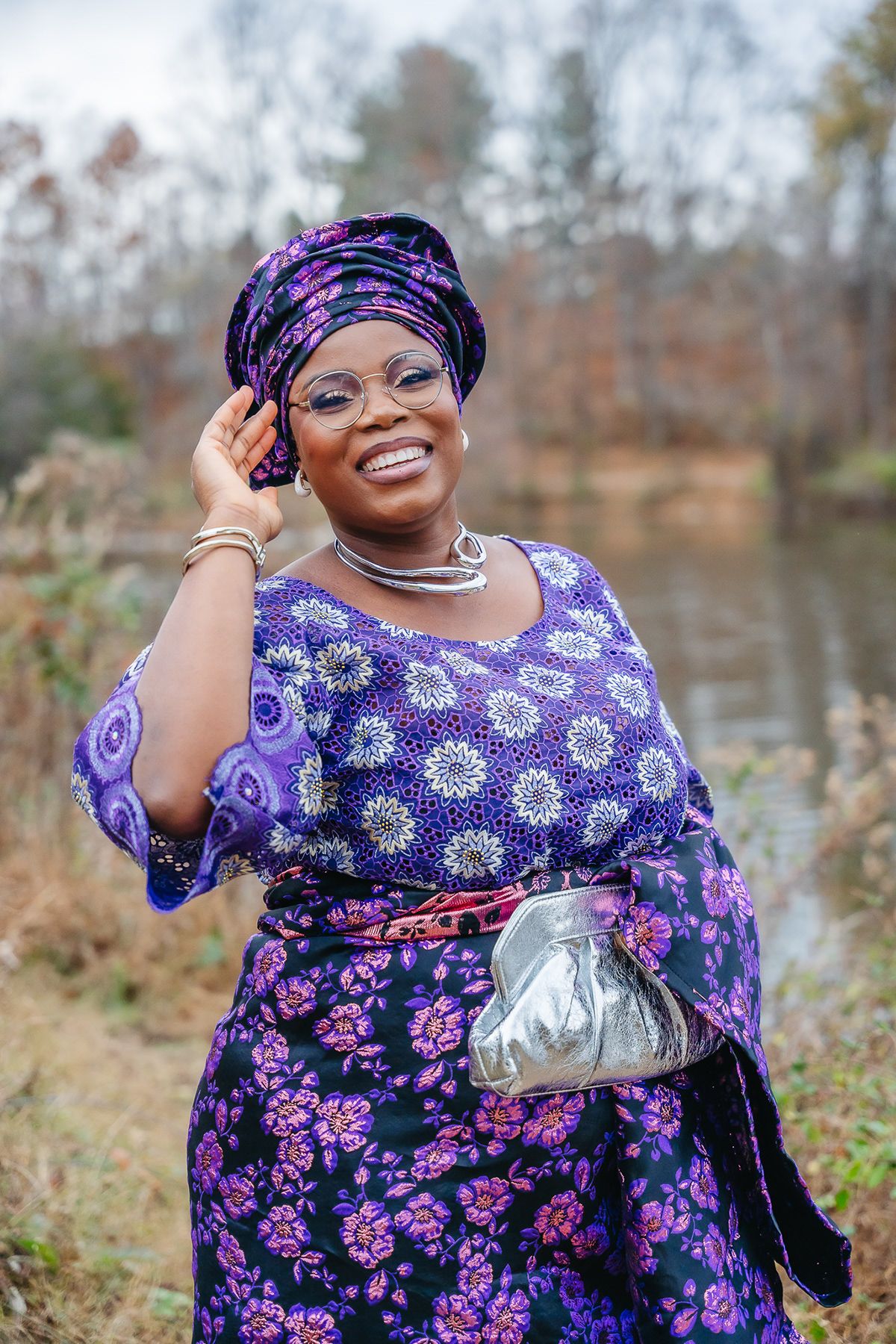 Beautiful purple and floral print dress with matching headwrap and silver accessories shown outdoors by a lake.