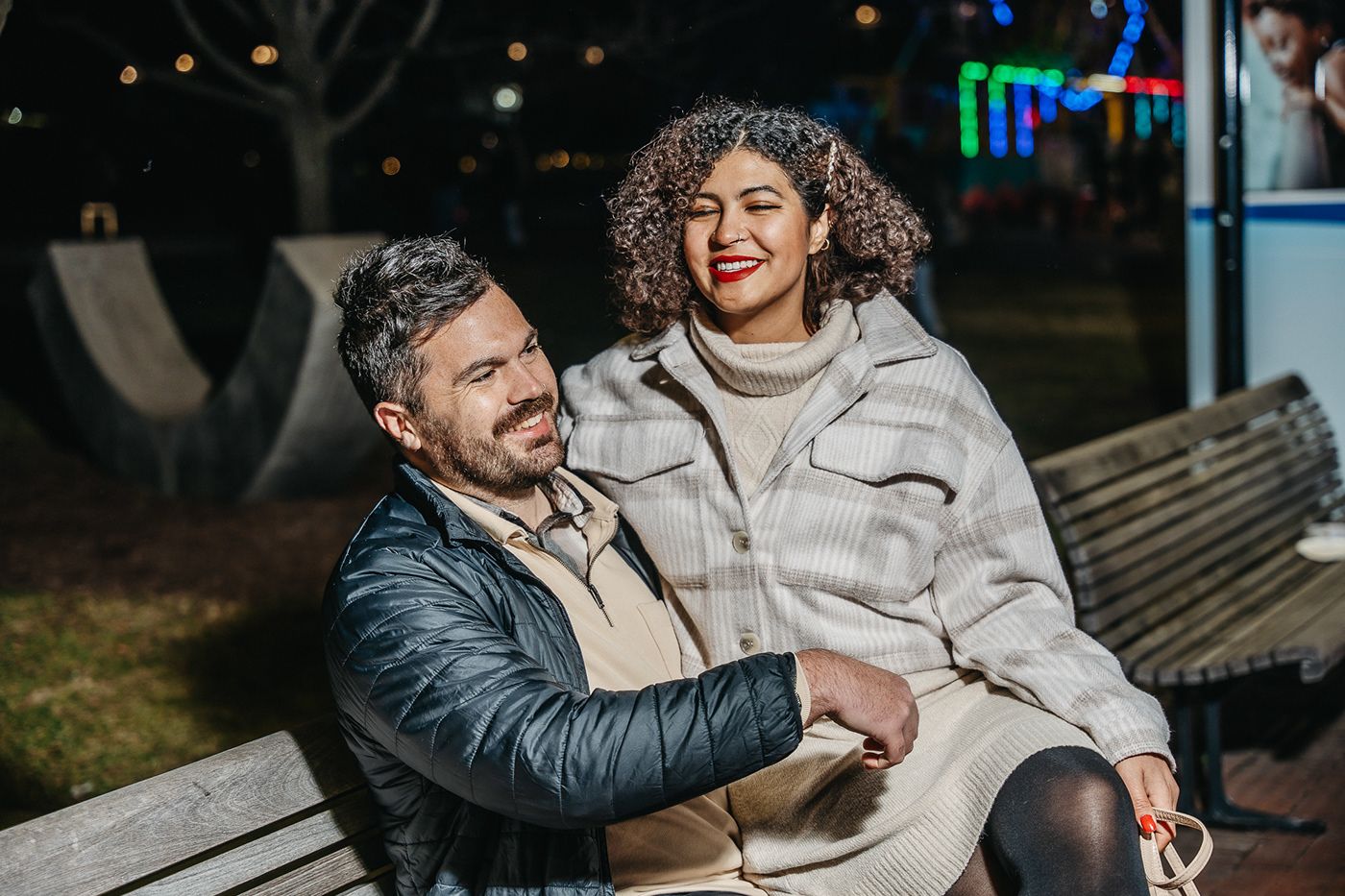 Happy couple laughing together while sitting on a bench at night.