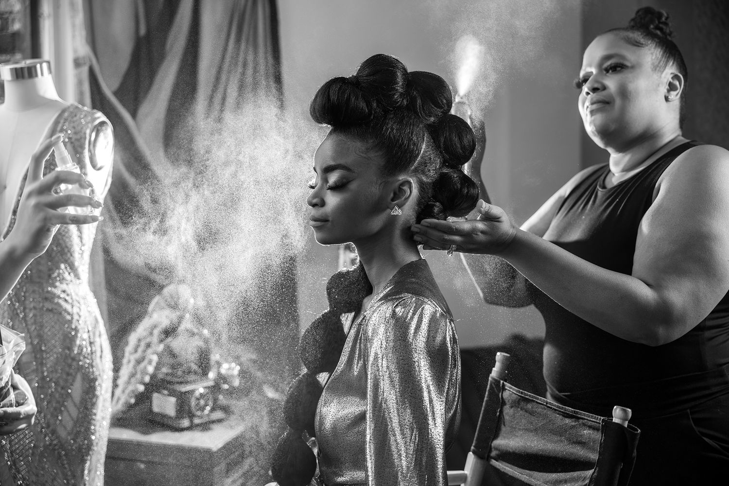 Black and white behind-the-scenes photo of hairstyling with dramatic lighting and mist.