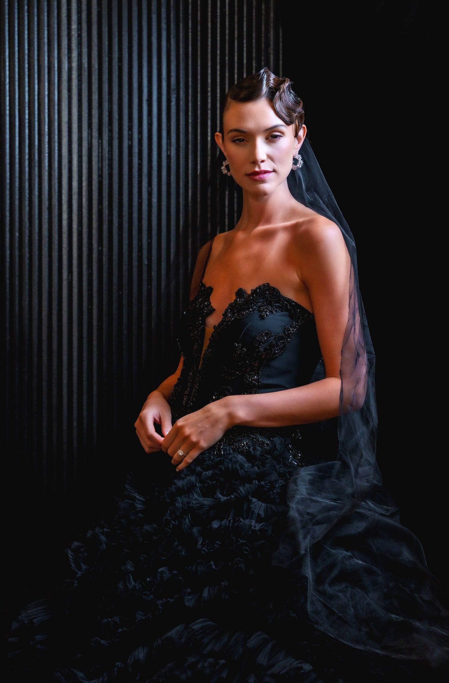 Elegant strapless black wedding dress with lace bodice and layered tulle skirt against dark backdrop.