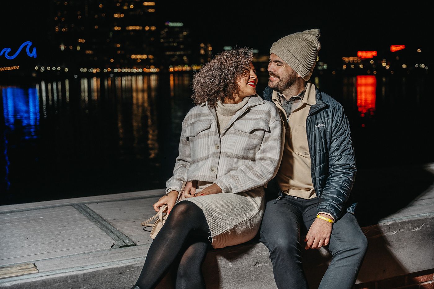 Couple enjoying a romantic evening by the waterfront with city lights reflecting on the water.