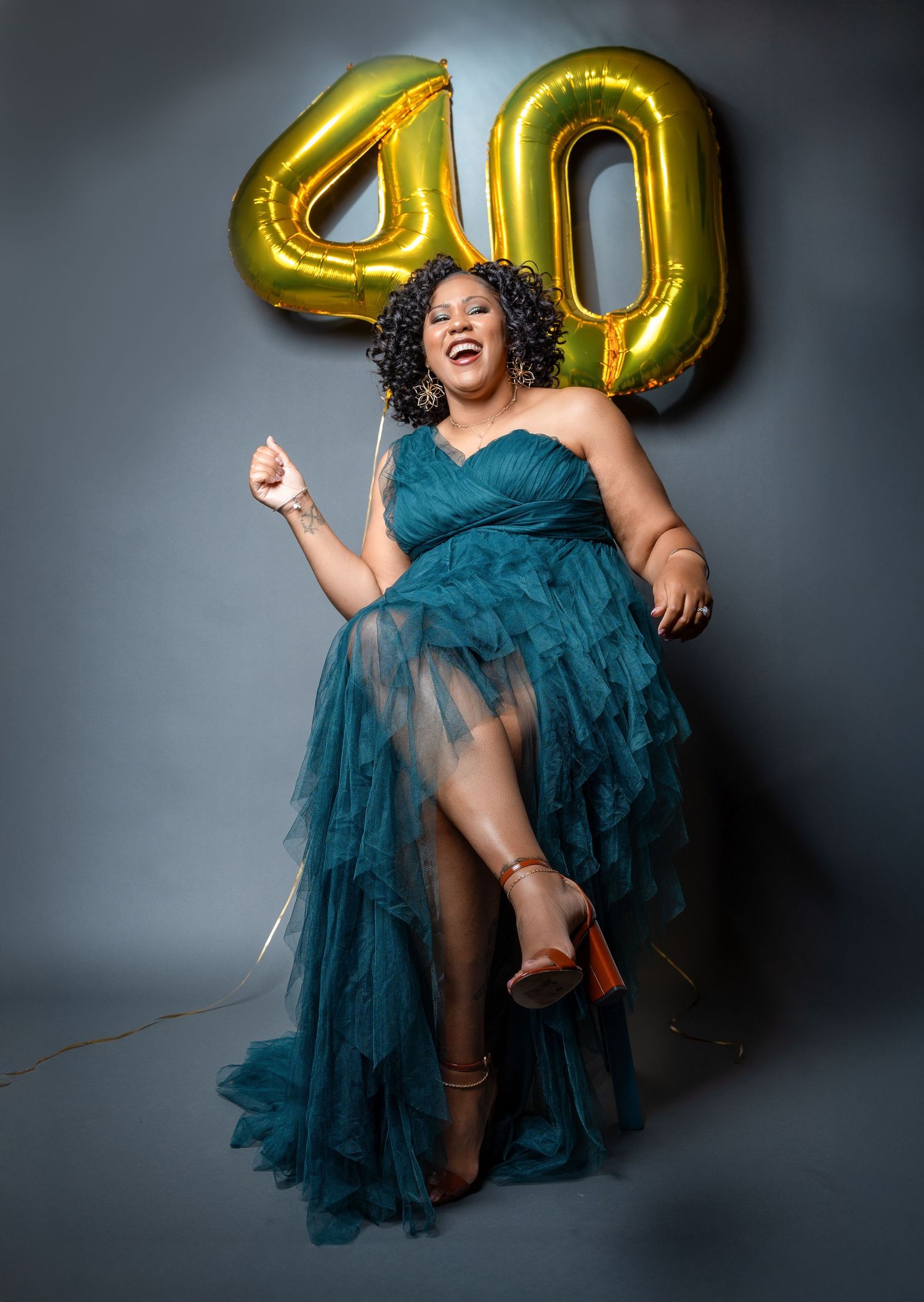 Celebratory photo with gold 40 balloons and teal tulle gown against grey background.