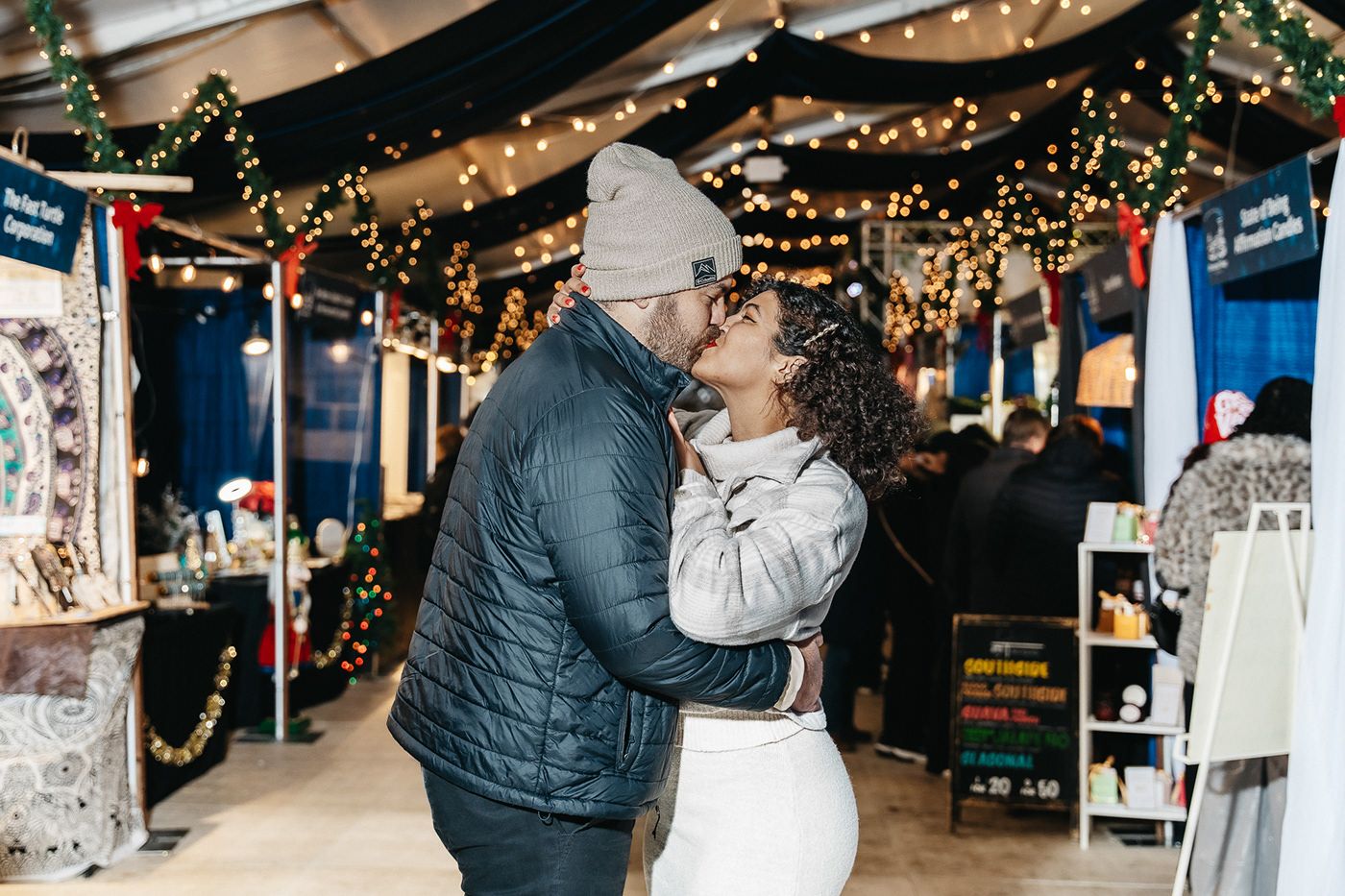 A couple shares a romantic moment under twinkling holiday lights in a decorated indoor space.