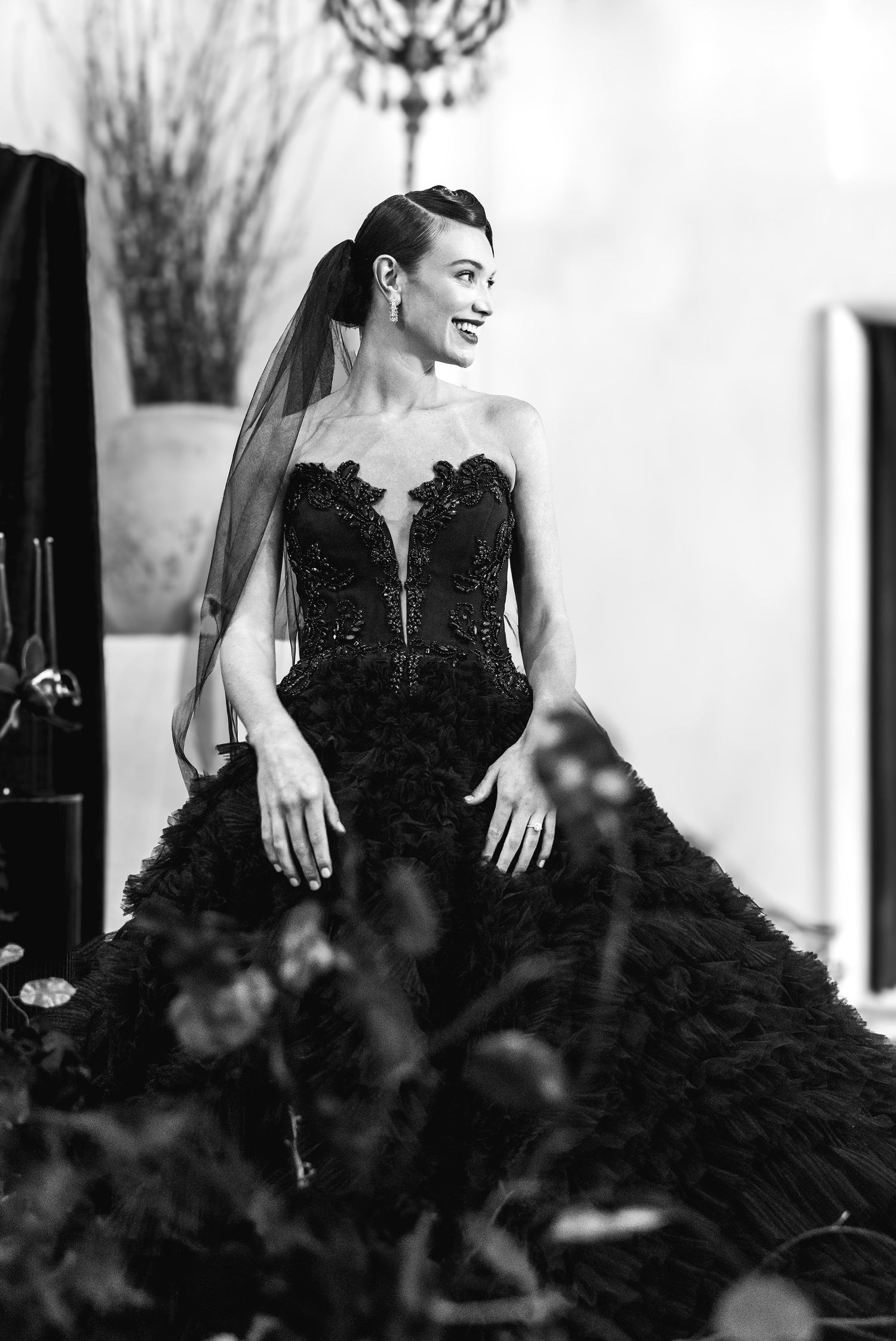 A bride in a dramatic black wedding gown with lace details and tulle skirt poses elegantly against a light background.