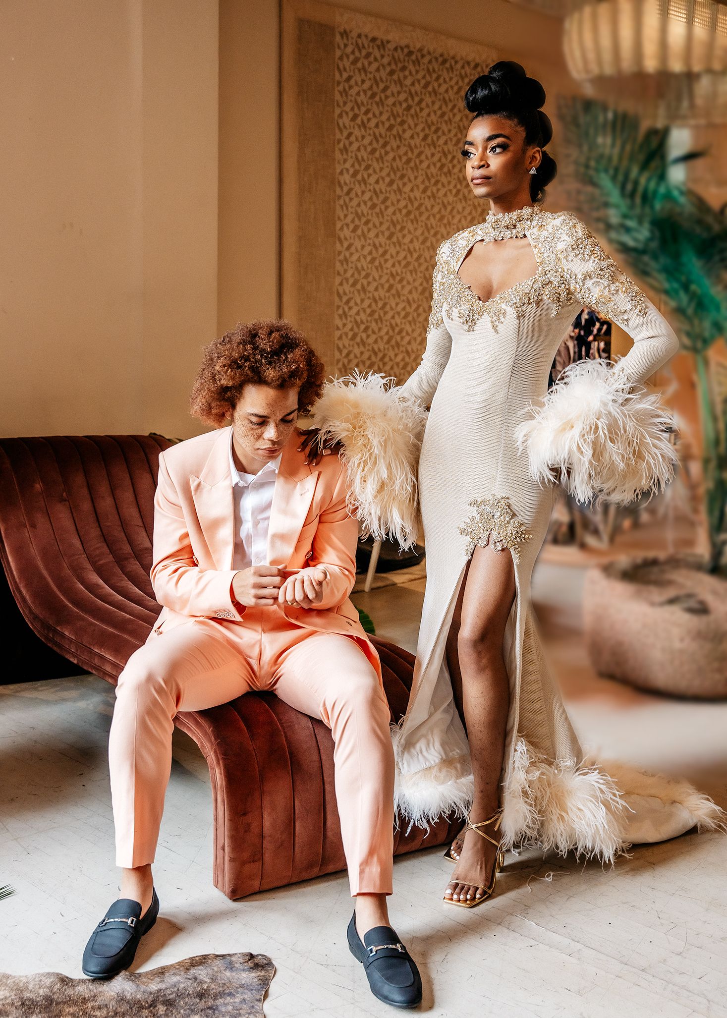 Elegant fashion shoot with white feathered dress and peach suit against vintage furniture.