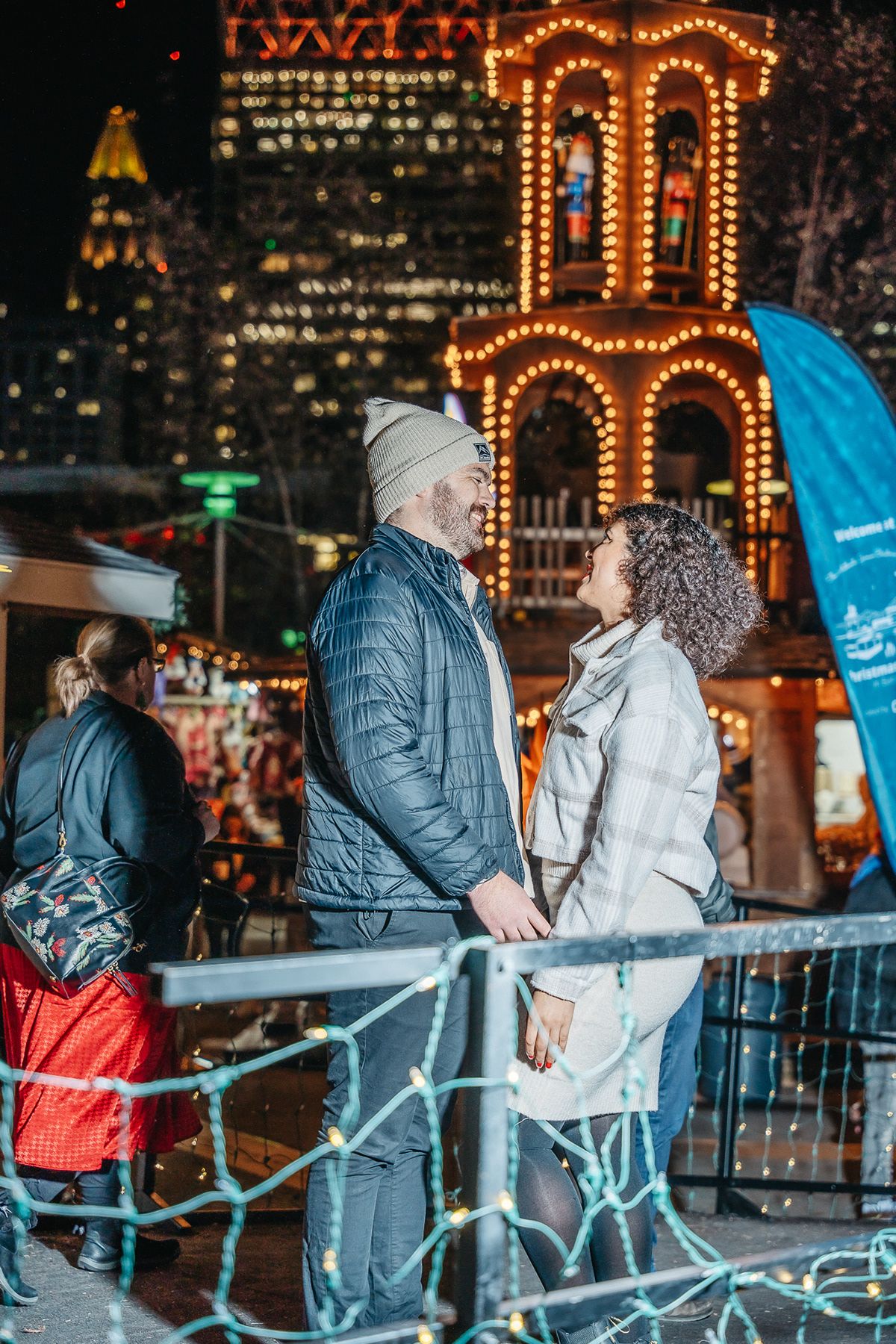 A couple enjoys a romantic moment near illuminated holiday decorations in an urban setting.