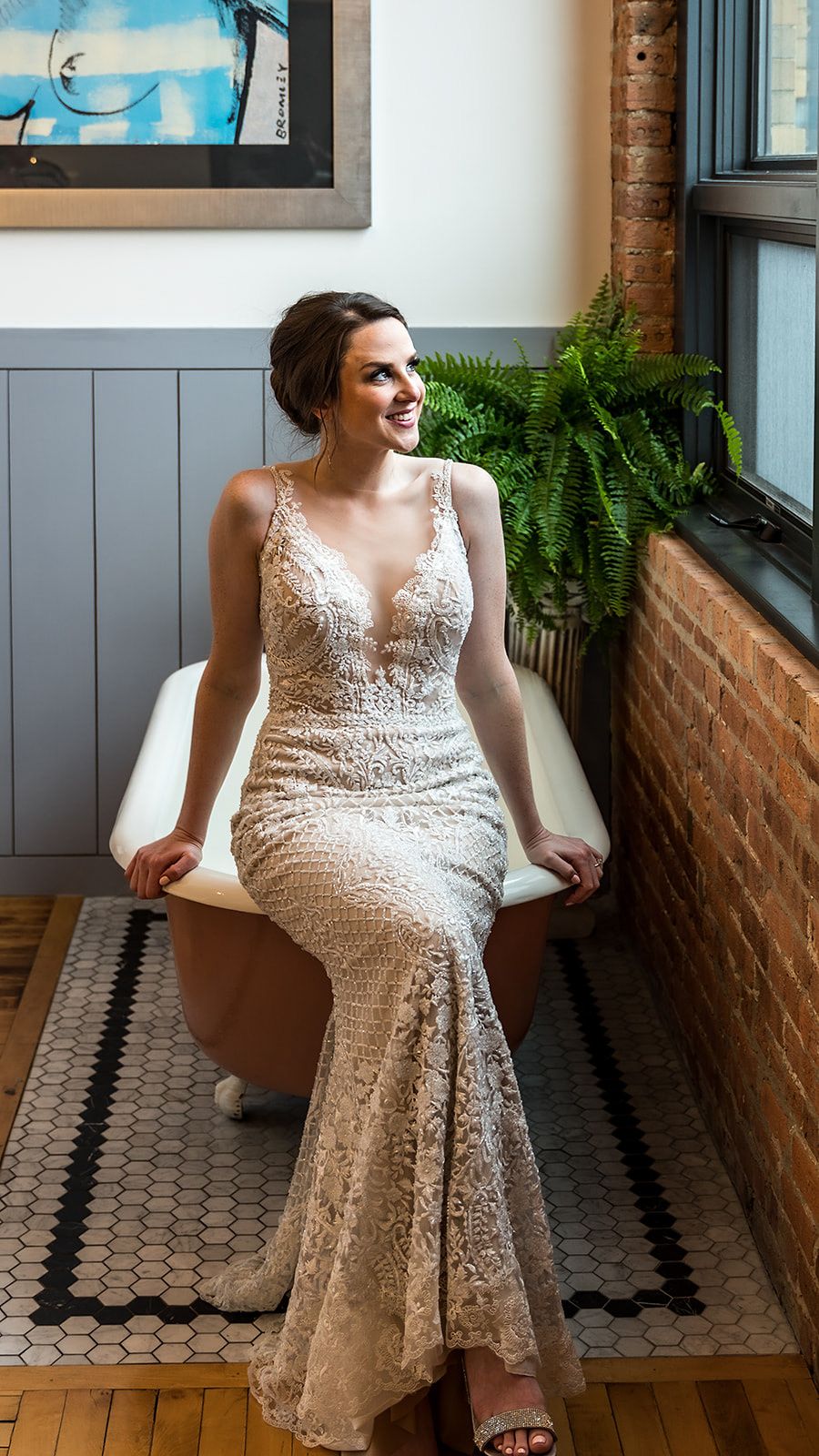 A stunning lace wedding dress with plunging neckline photographed in a room with exposed brick and ferns.