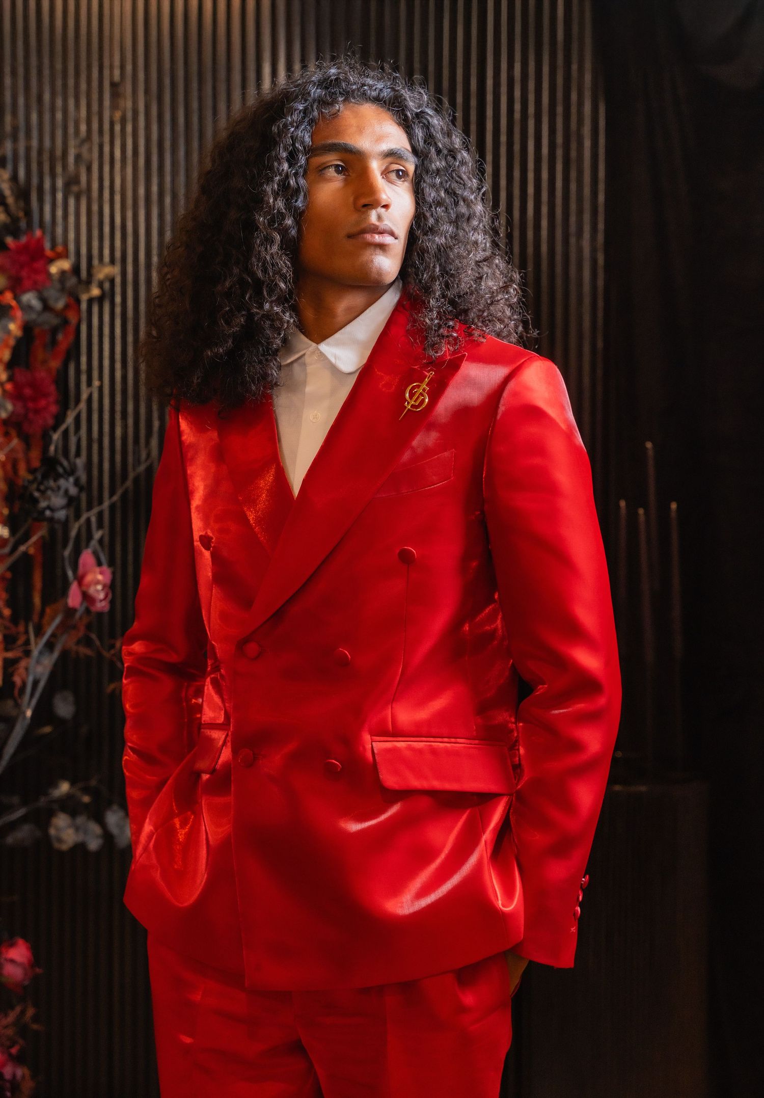 Stylish model in a vibrant red double-breasted suit with long curly hair against dark background.