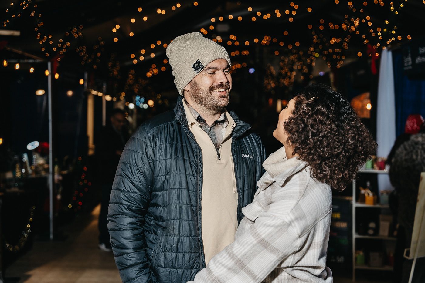 A couple shares a joyful moment together at night with twinkling lights in the background.