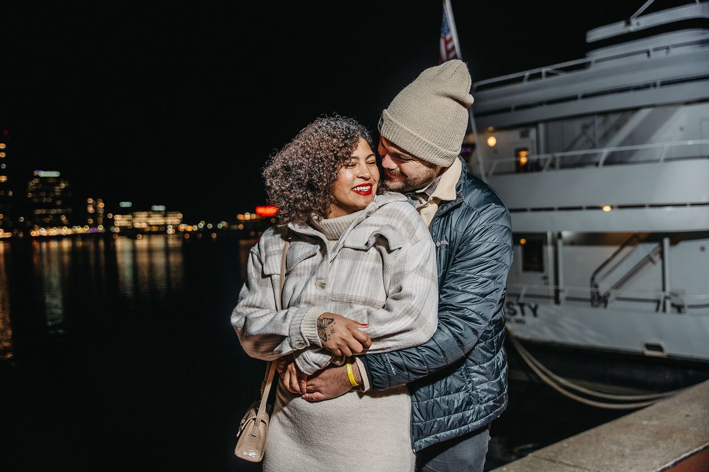 A romantic nighttime embrace by the waterfront with a yacht in the background.