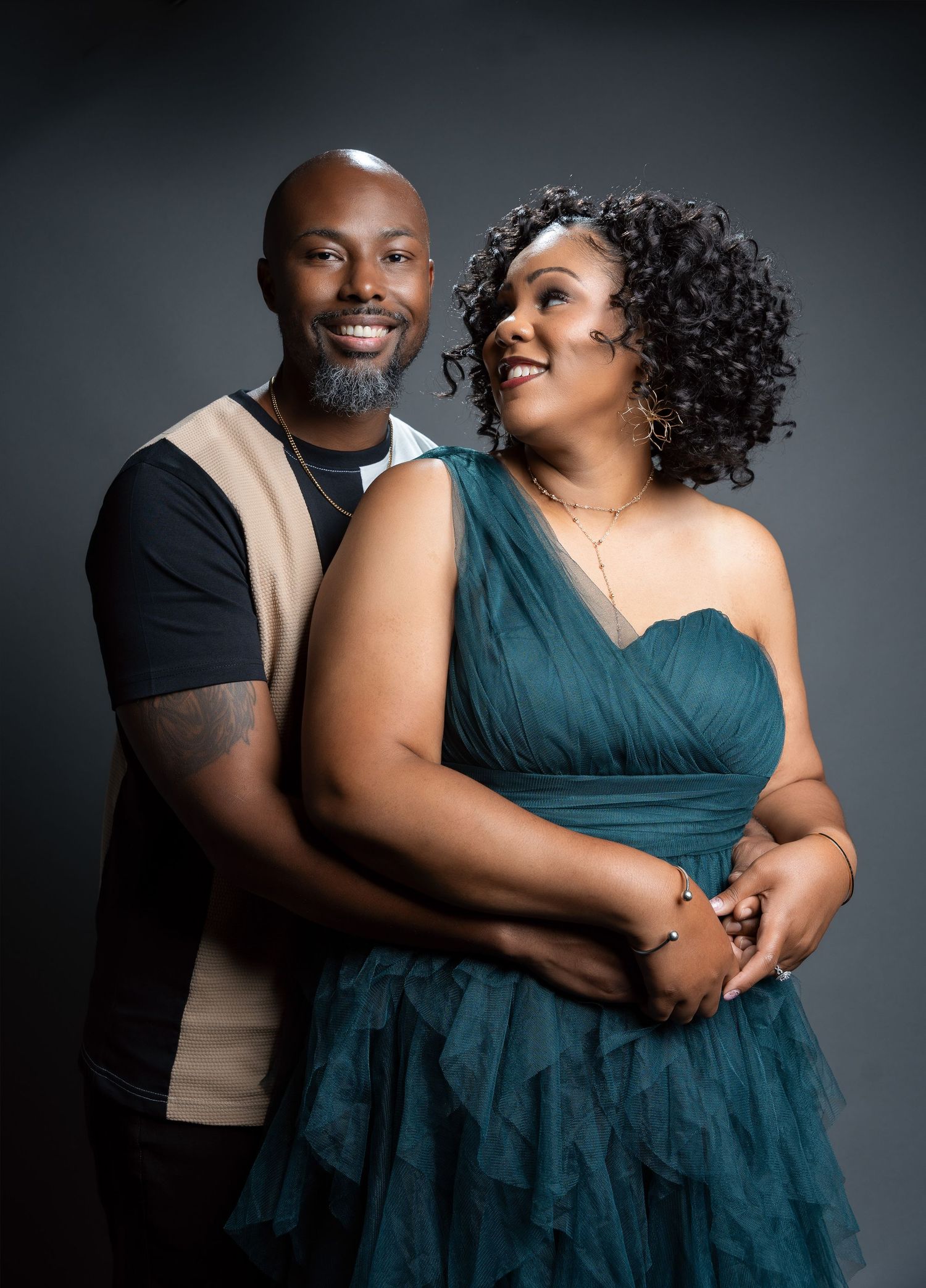 An elegant couple poses for a romantic studio portrait against a dark background.