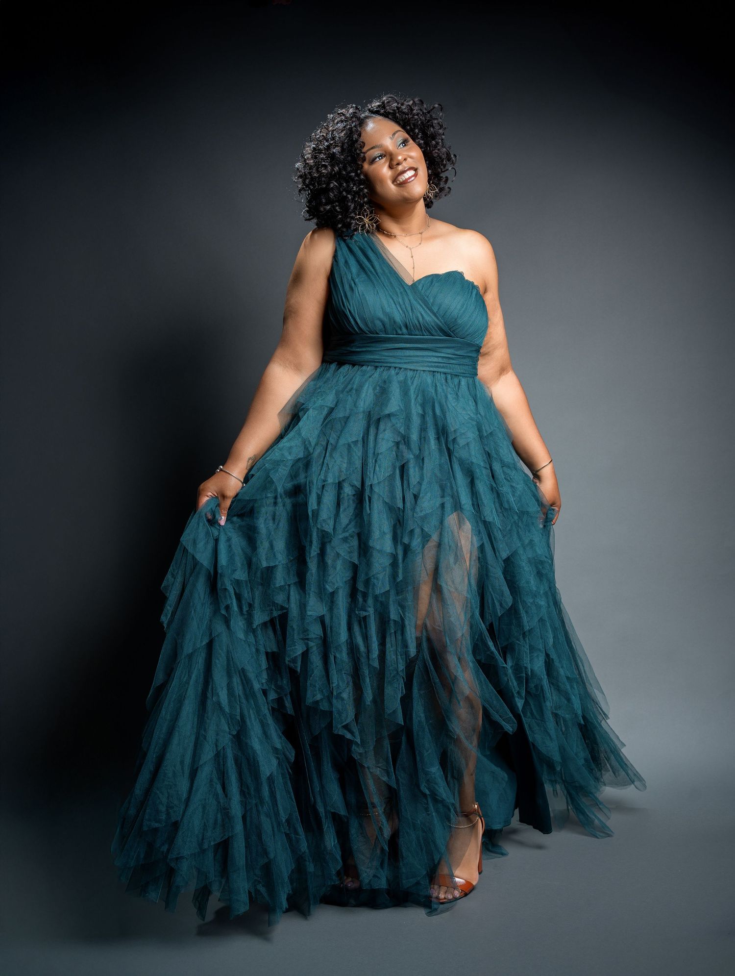 Fashion portrait featuring flowing teal evening gown against dark background.