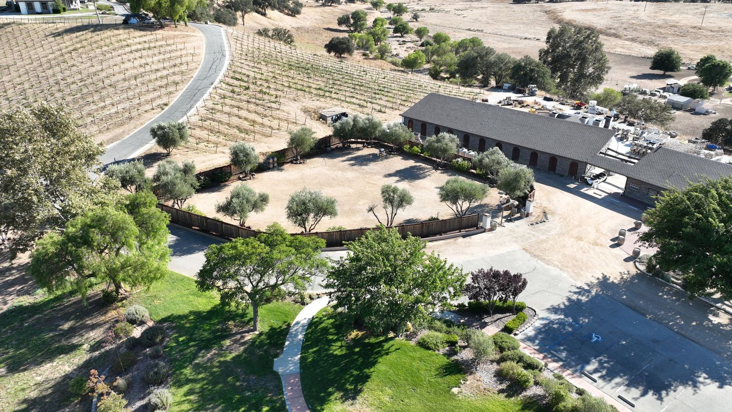Aerial view of a California winery estate with vineyard hillside, circular driveway, mature trees, and a ranch-style building.