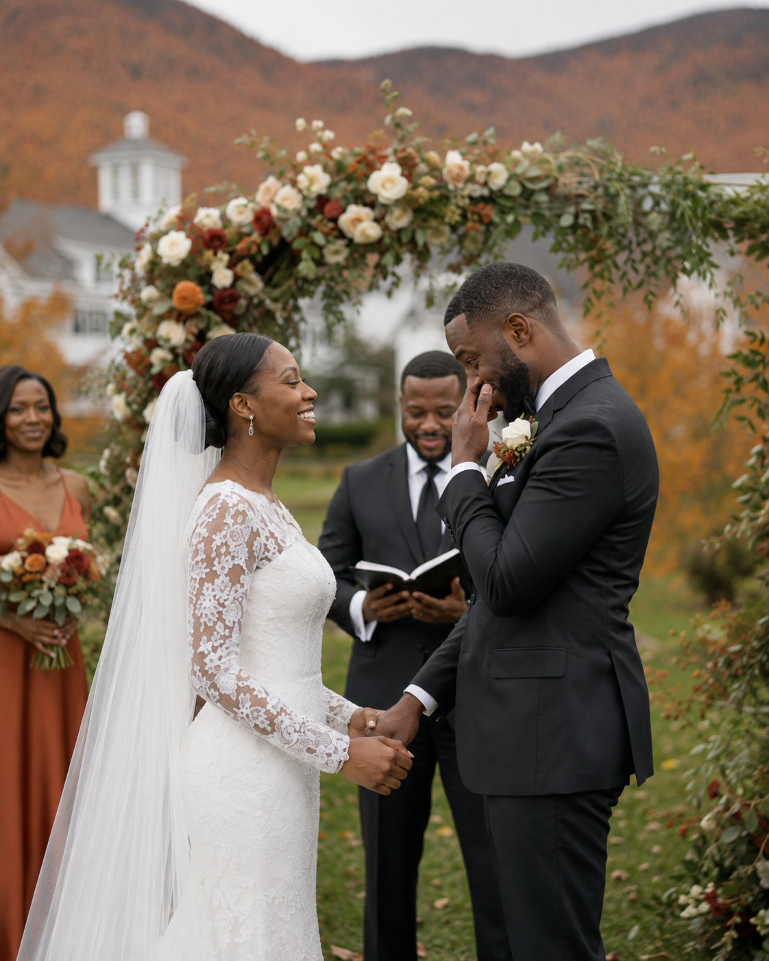 Emotional groom wipes tears as bride smiles during outdoor fall wedding ceremony with floral arch backdrop.