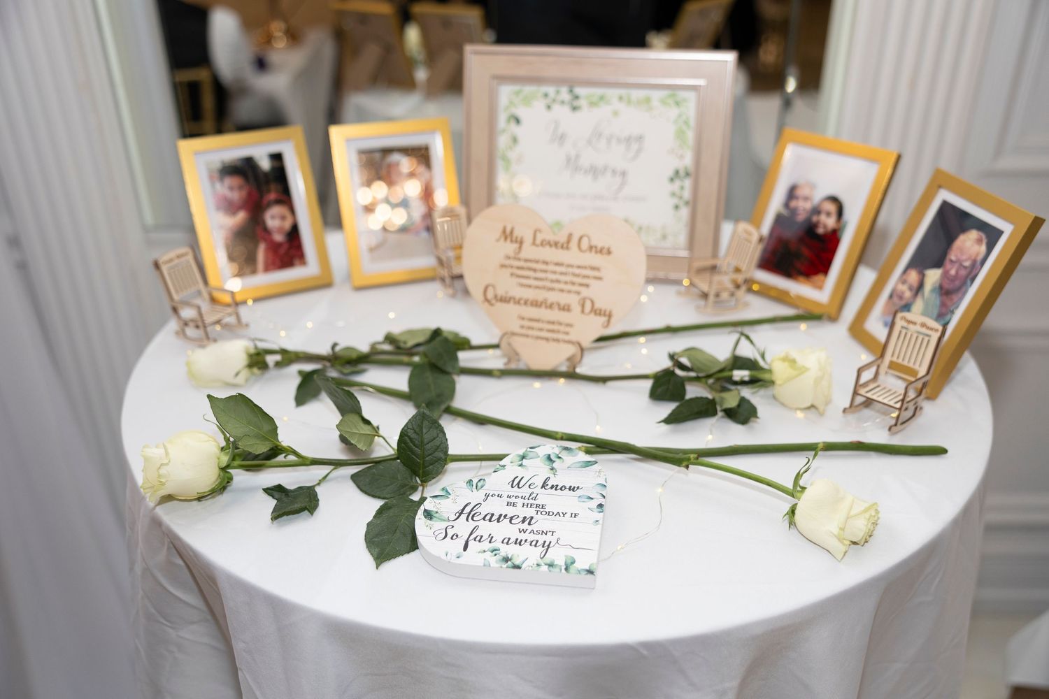 White table displays framed photographs and white roses arranged as a memorial or tribute display.