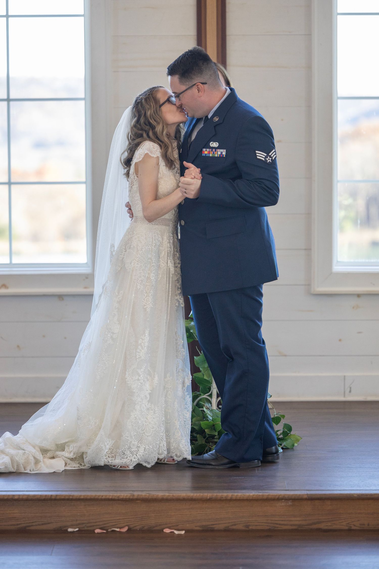 Military service member and bride share intimate dance moments in a bright sunlit venue with hardwood floors.