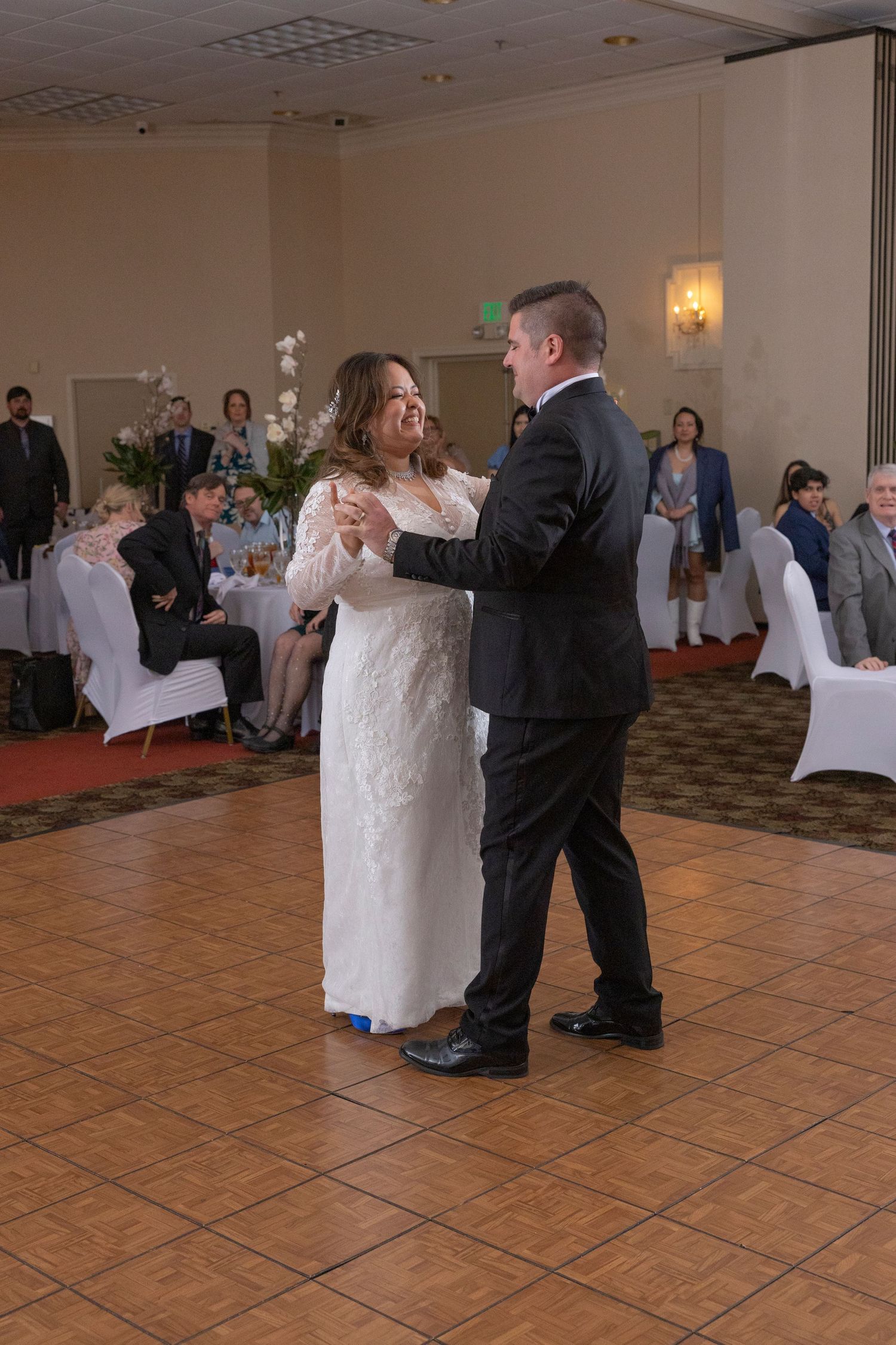 A couple shares their first dance at a wedding reception on a tiled dance floor in a banquet hall.