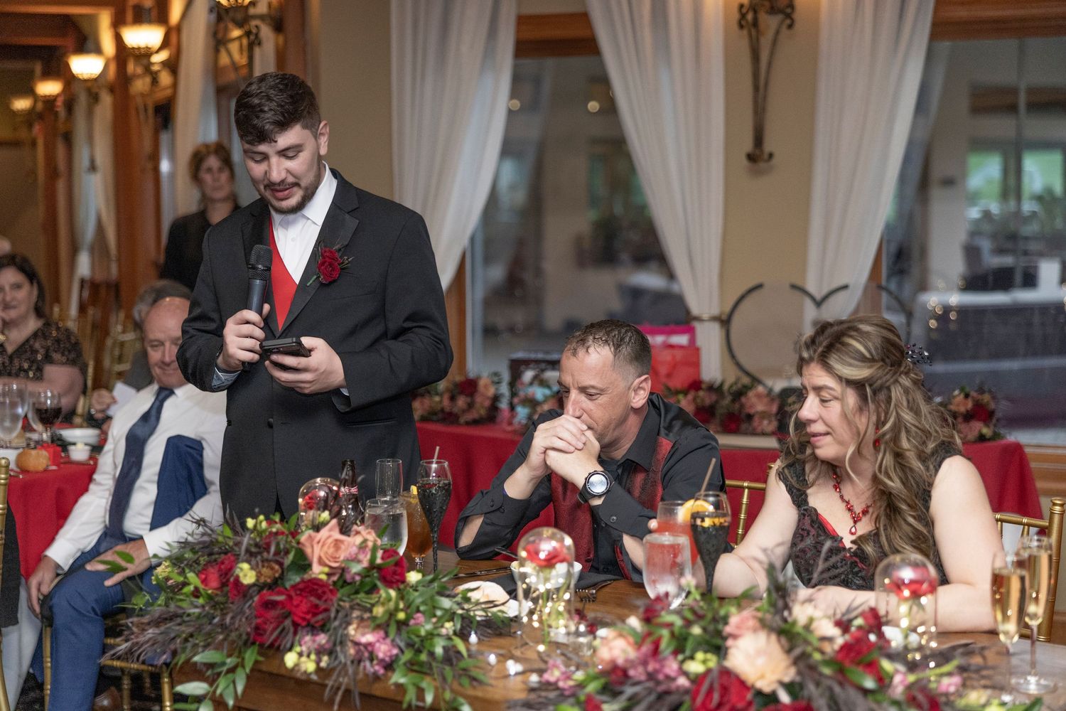 A long banquet table decorated with red floral centerpieces and candles at an elegant indoor reception.