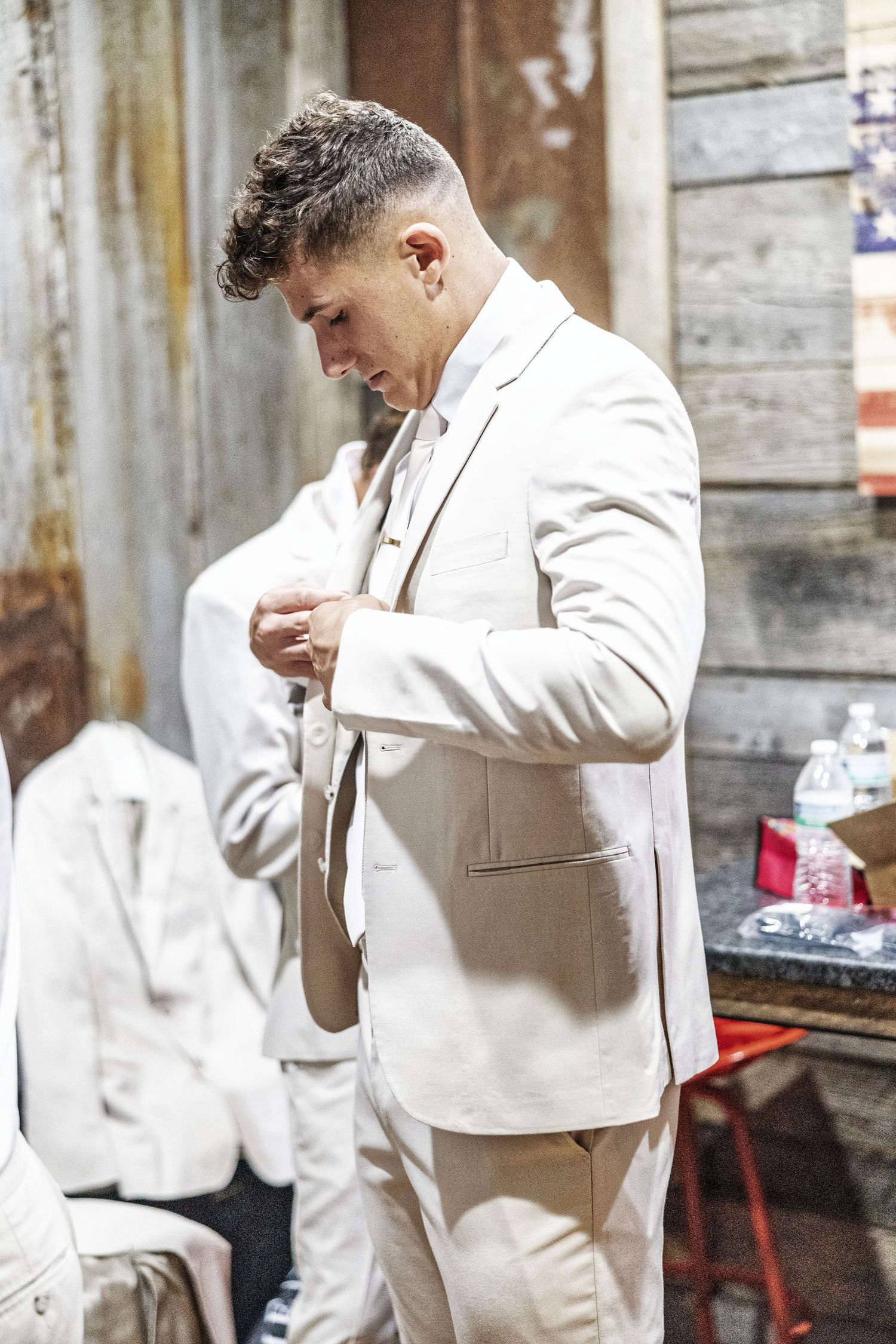 A person wearing an all-white outfit checks their phone while standing against a rustic wall.