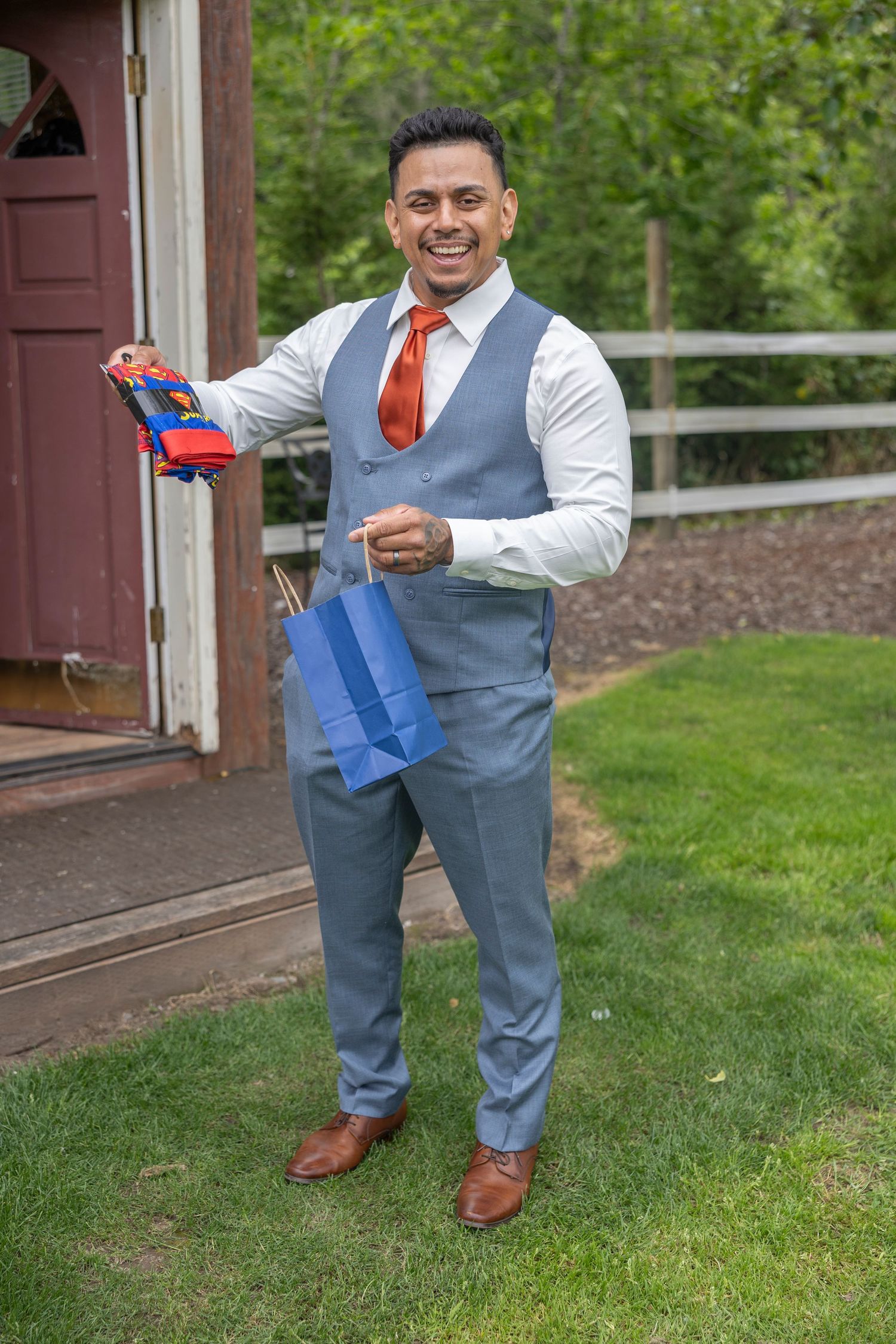 A person in a gray vest and white shirt playfully poses with a Nerf gun on a grassy lawn.