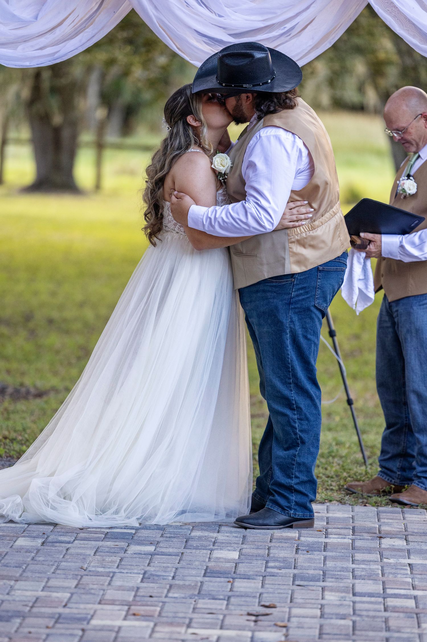 Romantic wedding couple embraces on stone paver patio with white tulle dress and cowboy boots in rustic outdoor setting.