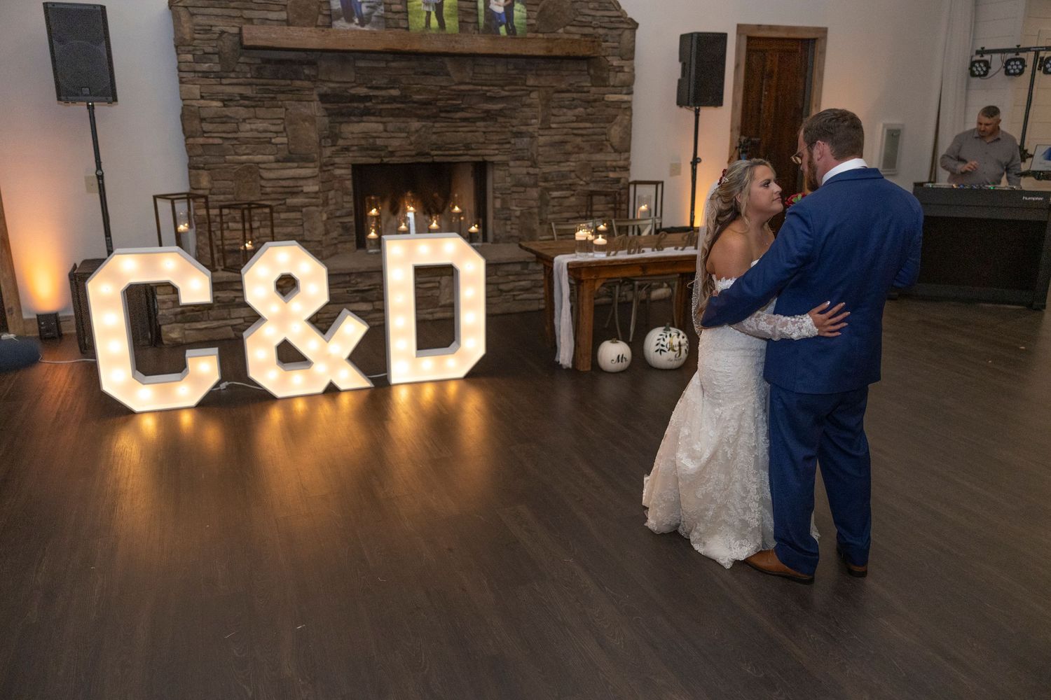 A couple dances together in a rustic venue with stone walls and illuminated letters in the background.