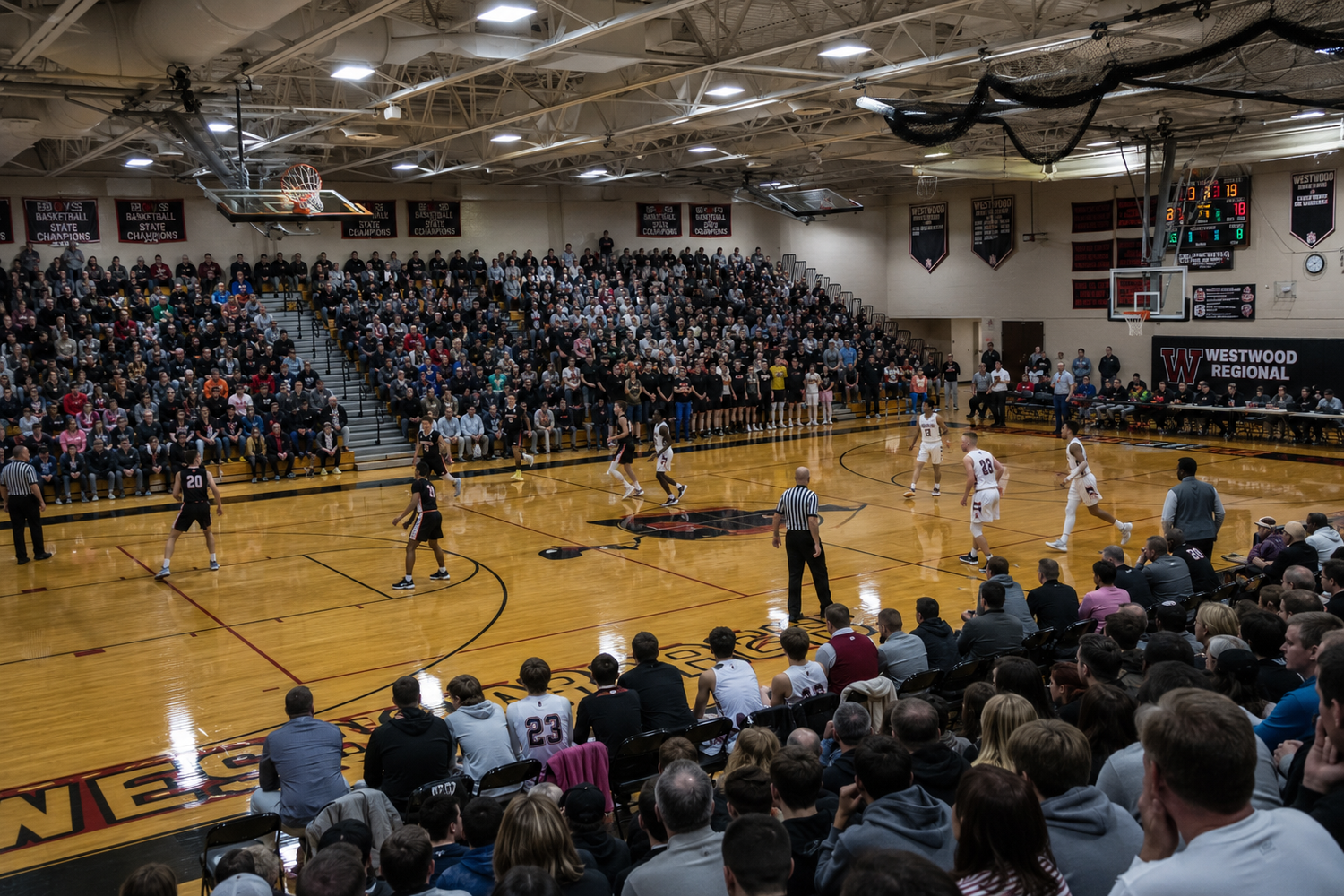 Packed high school basketball game with players on court and large crowd filling gymnasium bleachers.