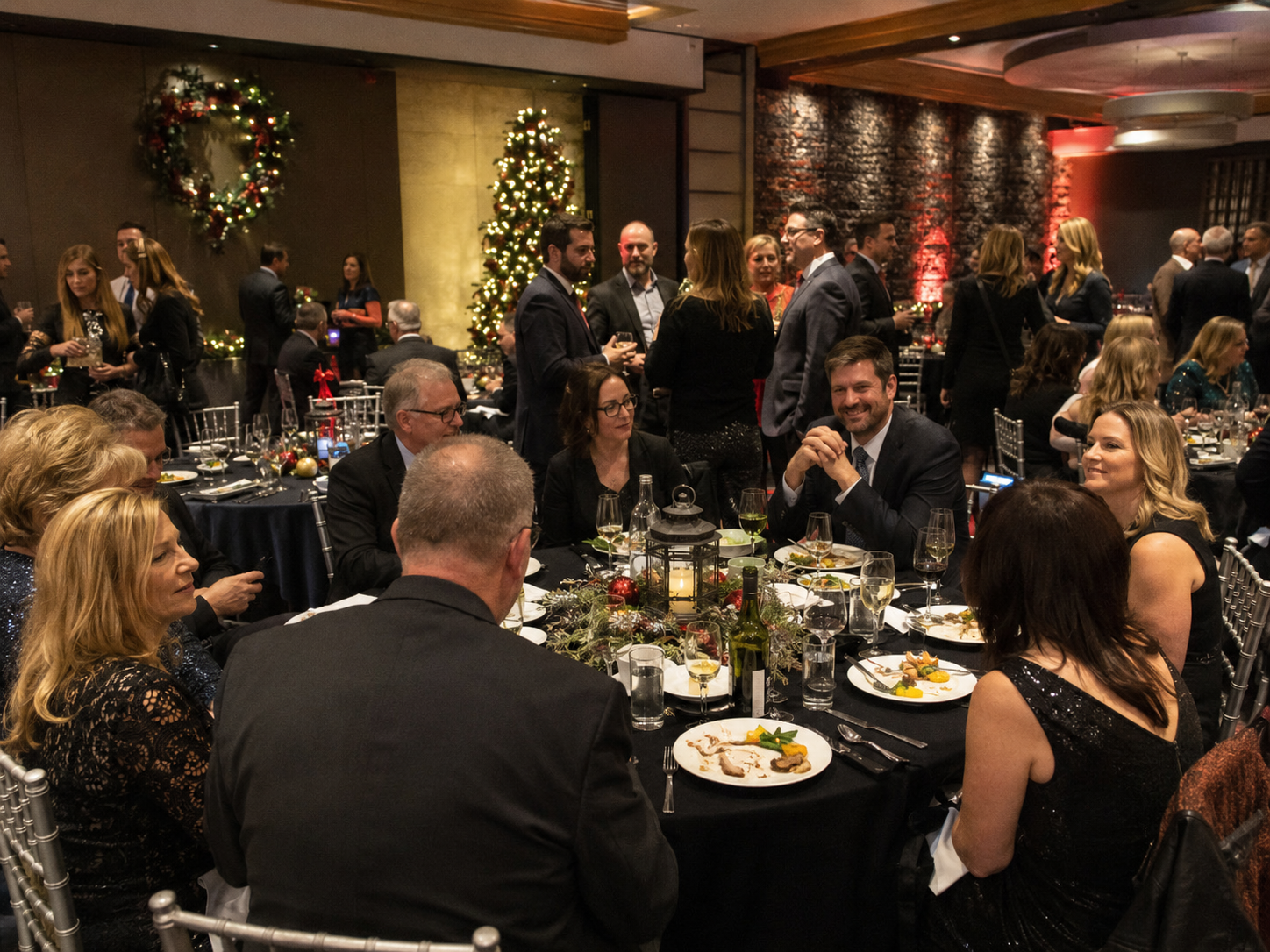 Elegantly dressed guests dining at round tables during a holiday gala event.