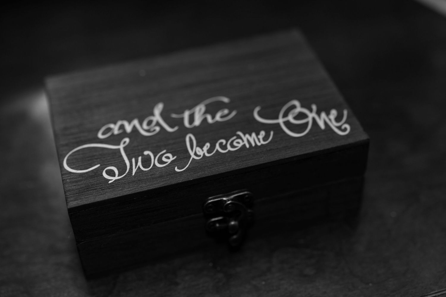 A black wooden box with cursive text reading 'and the two become one' engraved on its lid in white.