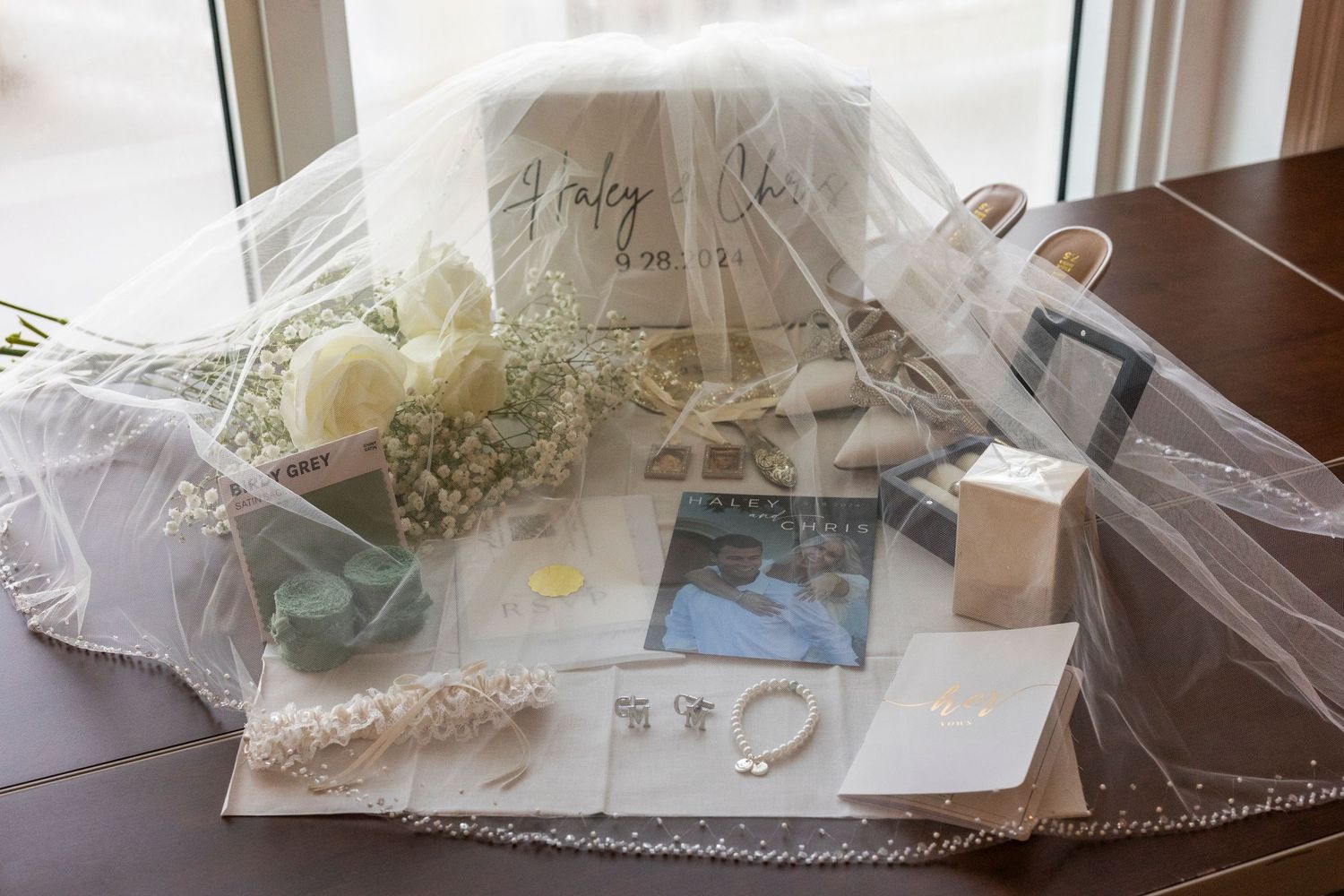 Wedding planning supplies including veil, lace trim, starfish decorations and photos spread on wooden table.