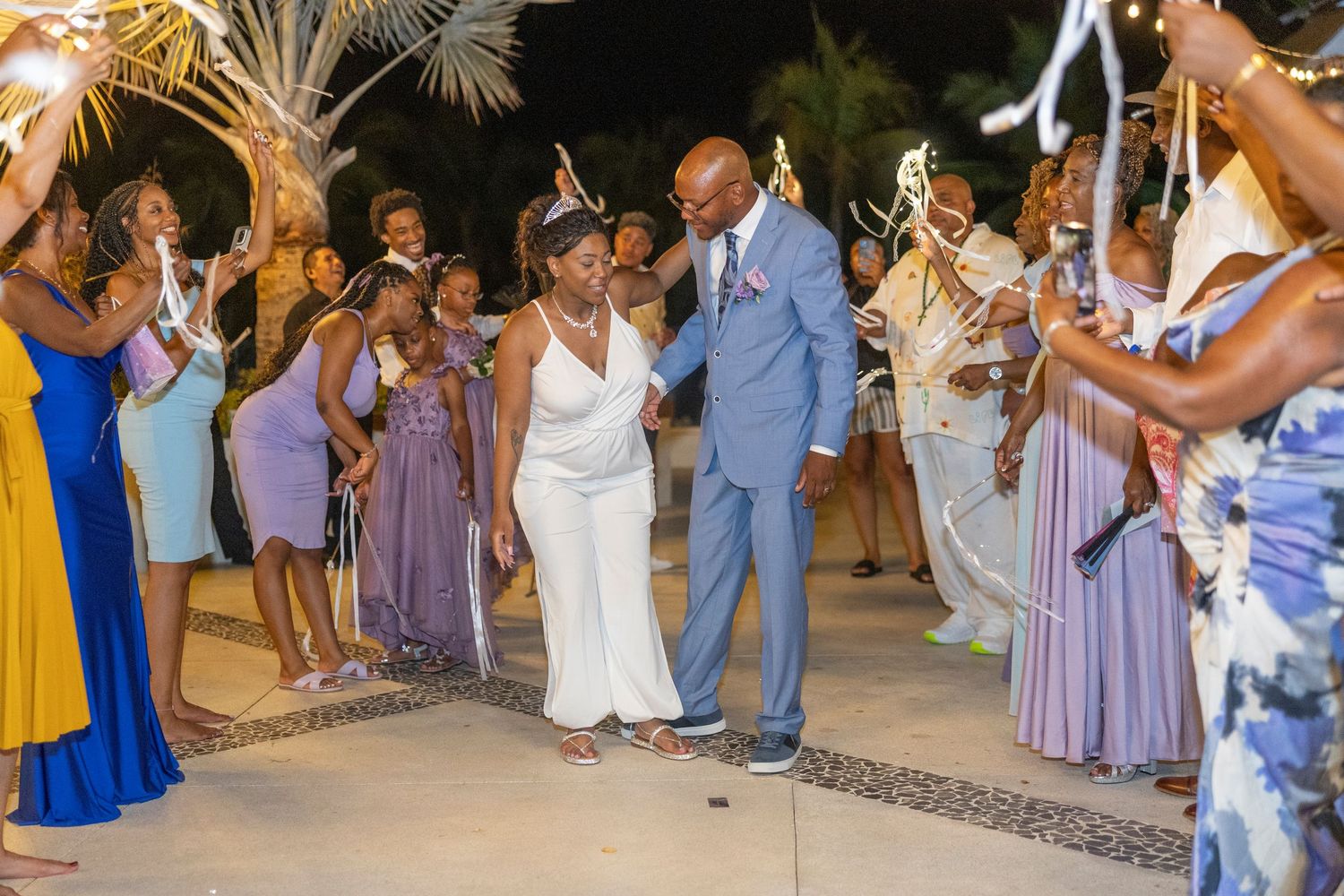 Wedding guests dance and celebrate at an outdoor reception with string lights illuminating the evening festivities.