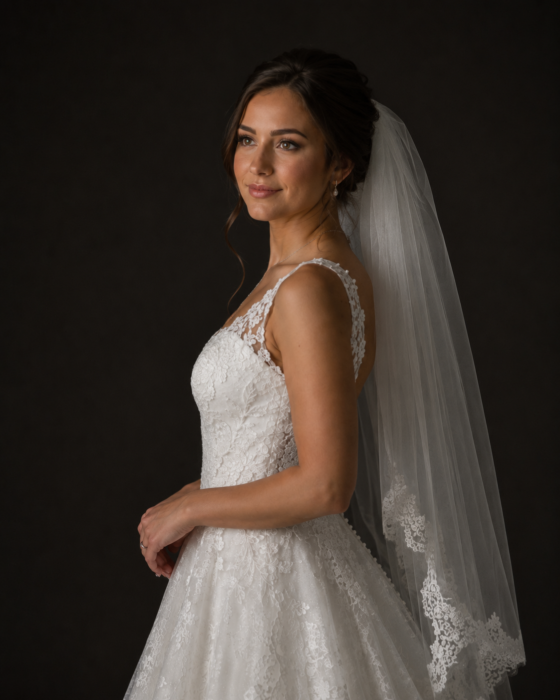 Close-up of bride in lace V-neck wedding dress with lace-edged veil, elegant updo, and soft bridal makeup.