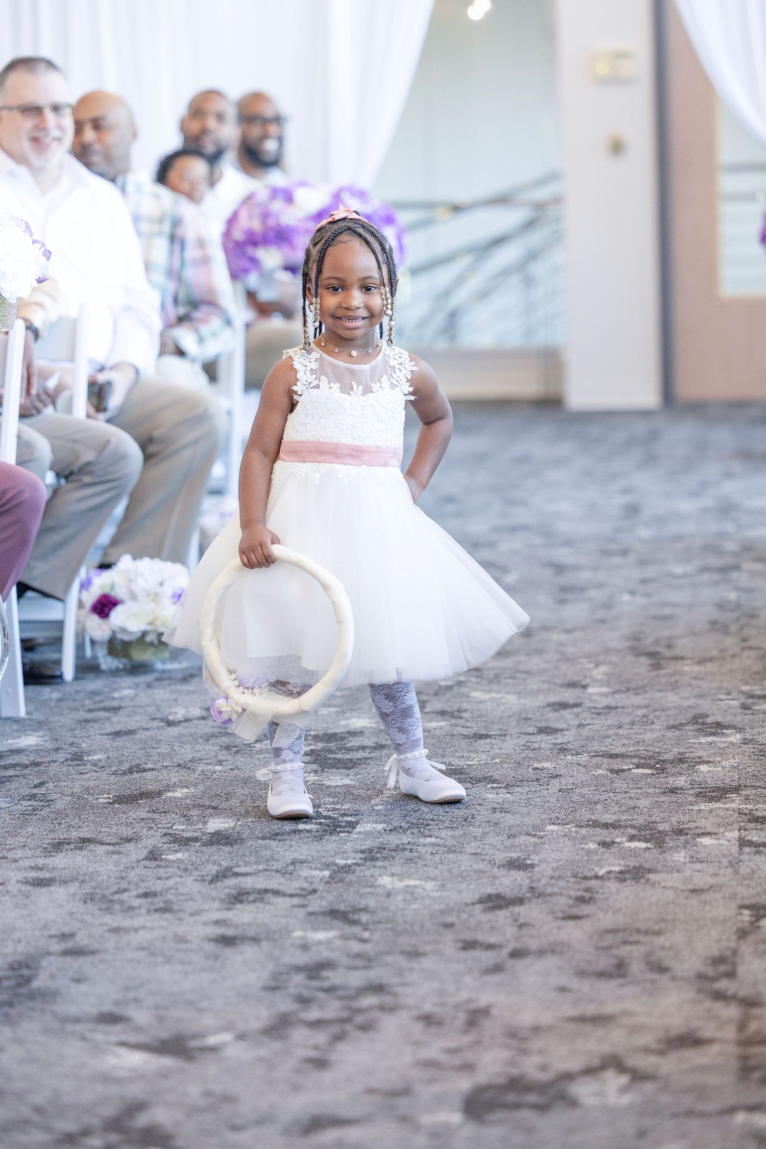 Adorable flower girl in white tutu dress holding a hoop walks down the aisle at an elegant wedding ceremony.