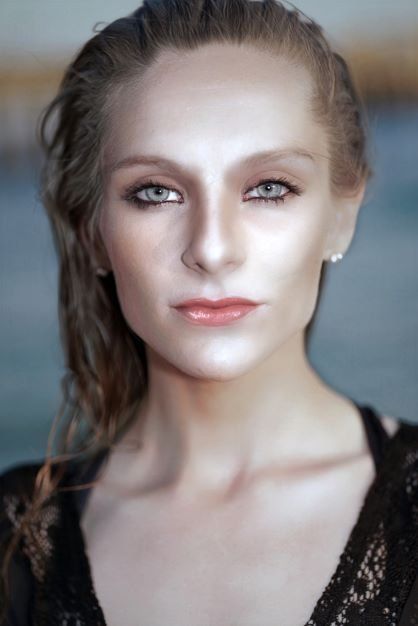 Close-up portrait of a young woman with smoky eye makeup, pearl earring, and sleek hair in black lace top.