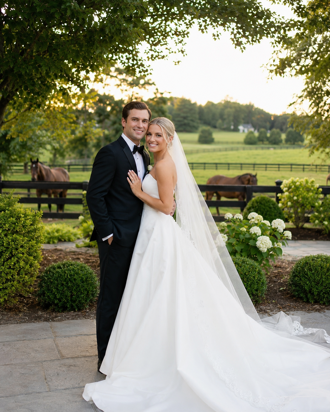 Bride and groom pose together in a lush garden wedding venue with horses and green fields in the background.