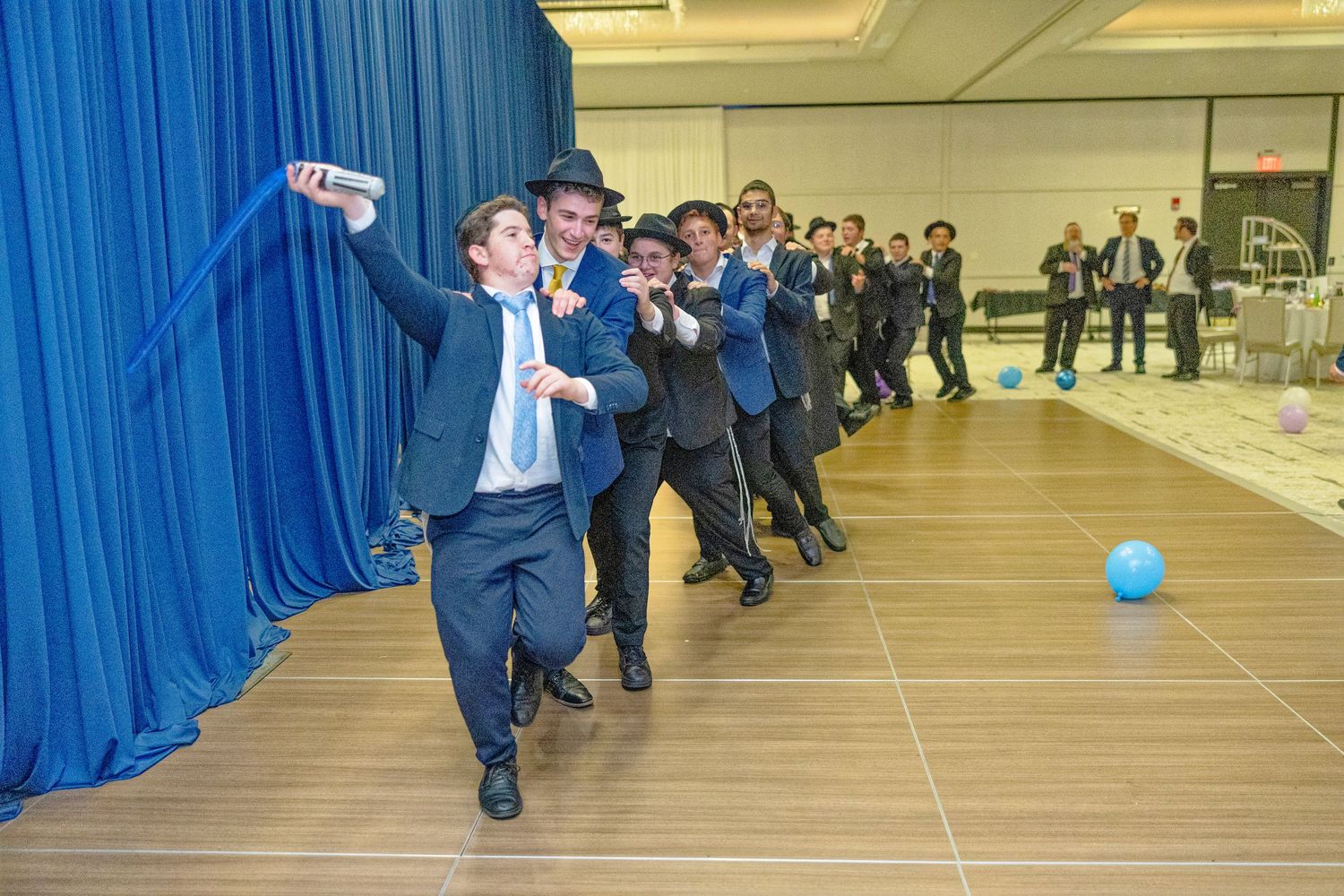 People in formal attire playing an indoor team building game with a blue balloon in a large conference room.