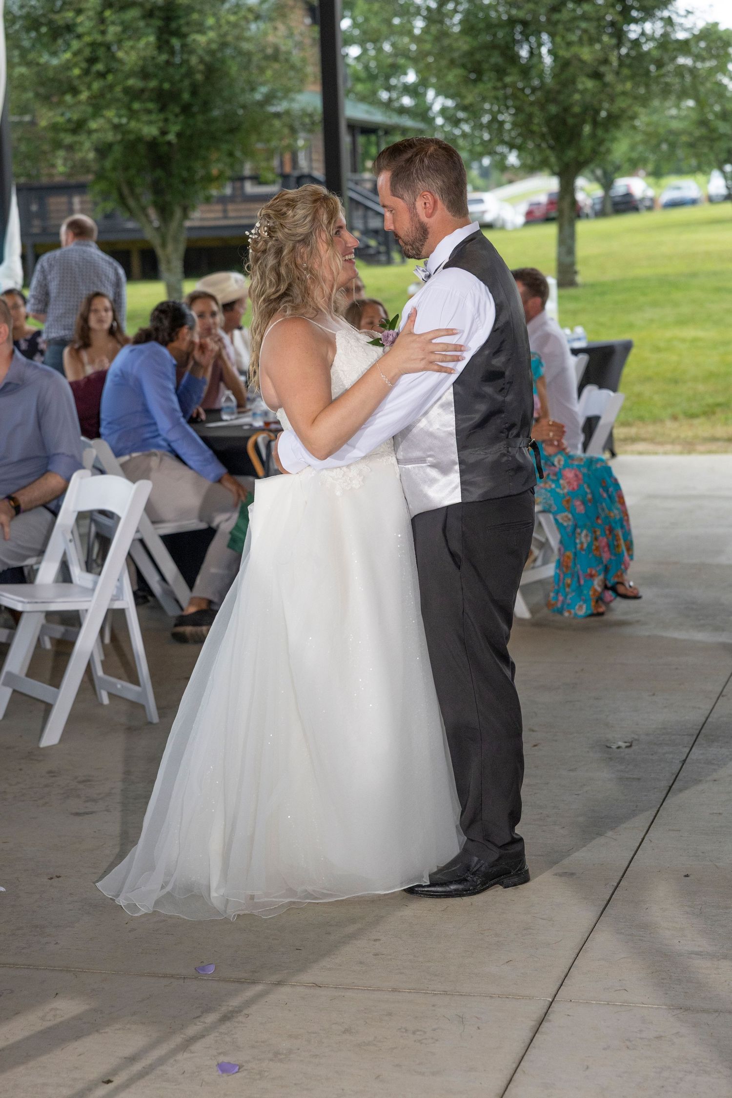 A couple shares their first dance as newlyweds at an outdoor wedding reception under a covered pavilion.