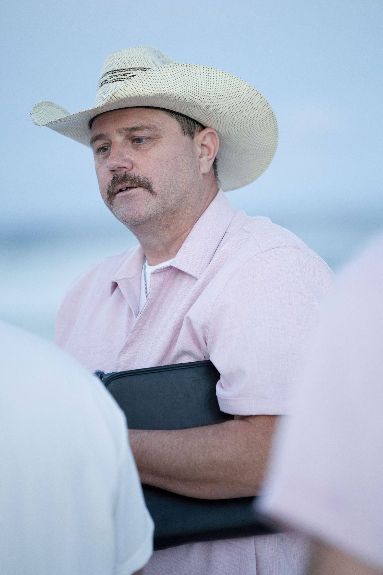 A person in a white cowboy hat and pink shirt stands against a light background.