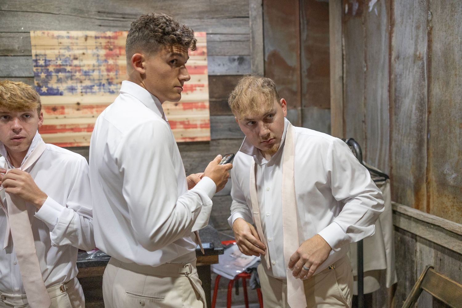 Three people in white uniforms stand together checking their phones and devices in a rustic setting.