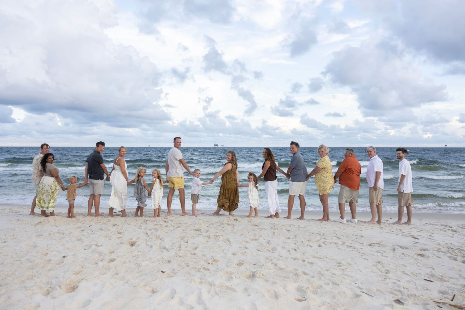 A group of people walking in a line along a sandy beach with ocean waves and cloudy sky in the background.