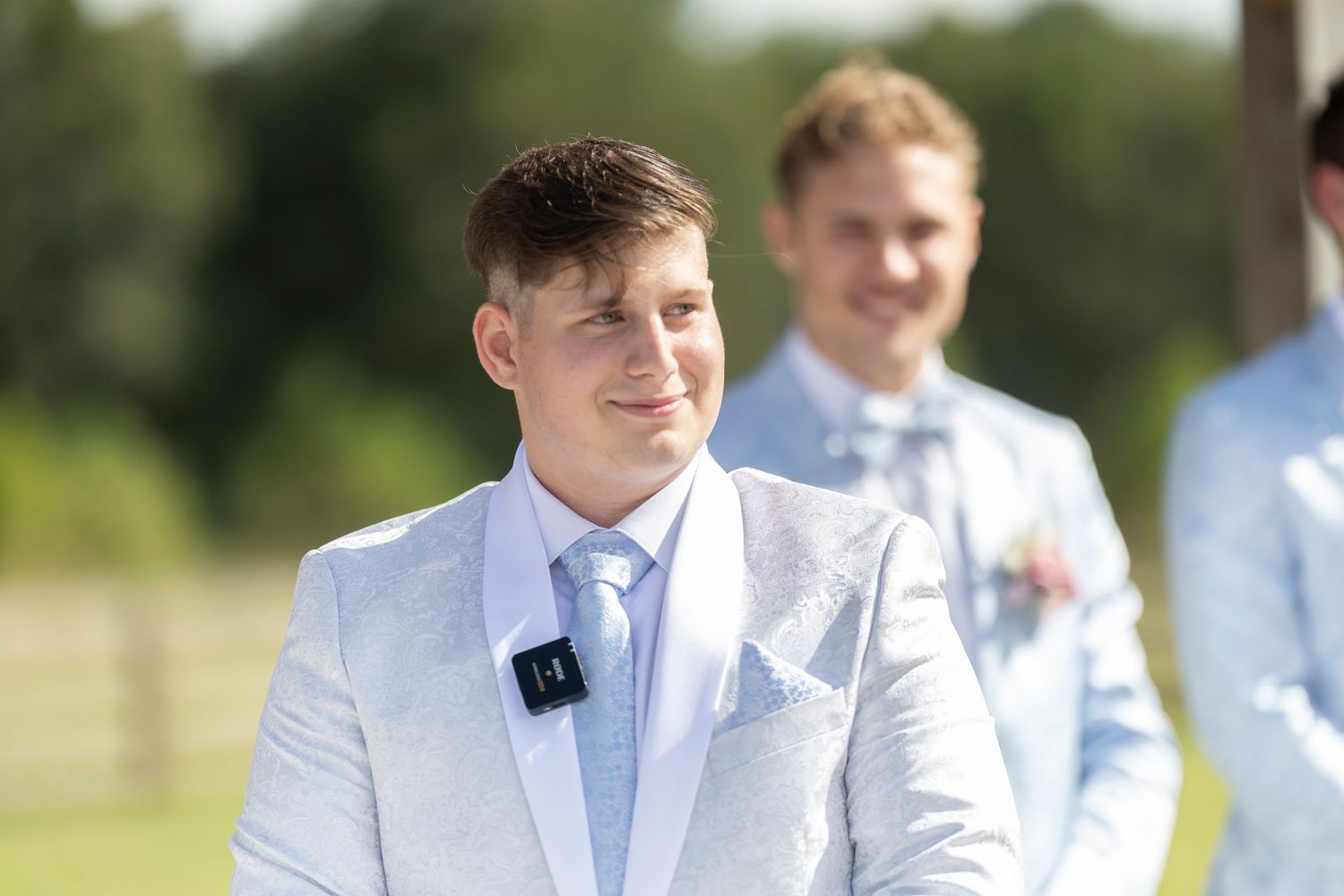 A group of groomsmen in light blue and white suits smile and laugh together outdoors.