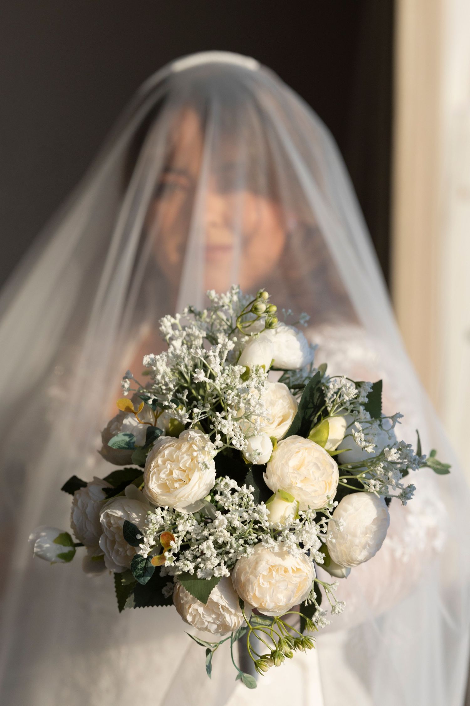 A romantic bridal bouquet featuring white garden roses, baby's breath and eucalyptus leaves behind a delicate veil.